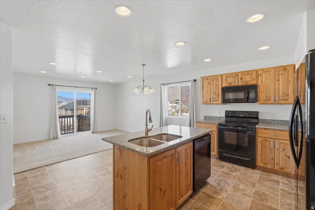 Kitchen featuring black appliances, light stone counters, a textured ceiling, stone finish floors, and a center island with sink