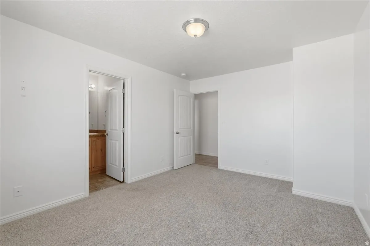 Unfurnished bedroom featuring light carpet and connected bathroom