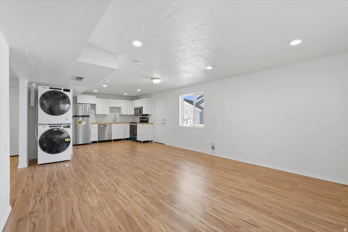 Laundry area with light wood-type flooring, stacked washer and dryer, and recessed lighting