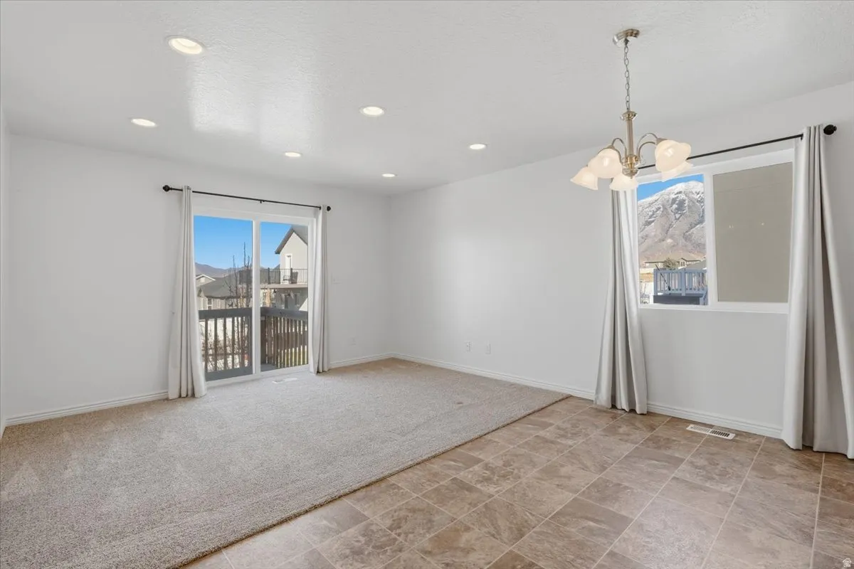 Unfurnished room with suspended lighting, stone finish flooring, healthy amount of natural light, and light carpet