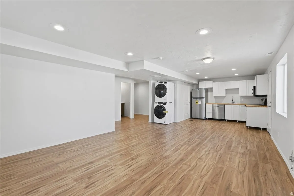 Kitchen featuring white cabinets, recessed lighting, light wood-style floors, stacked washer / dryer, and stainless steel appliances