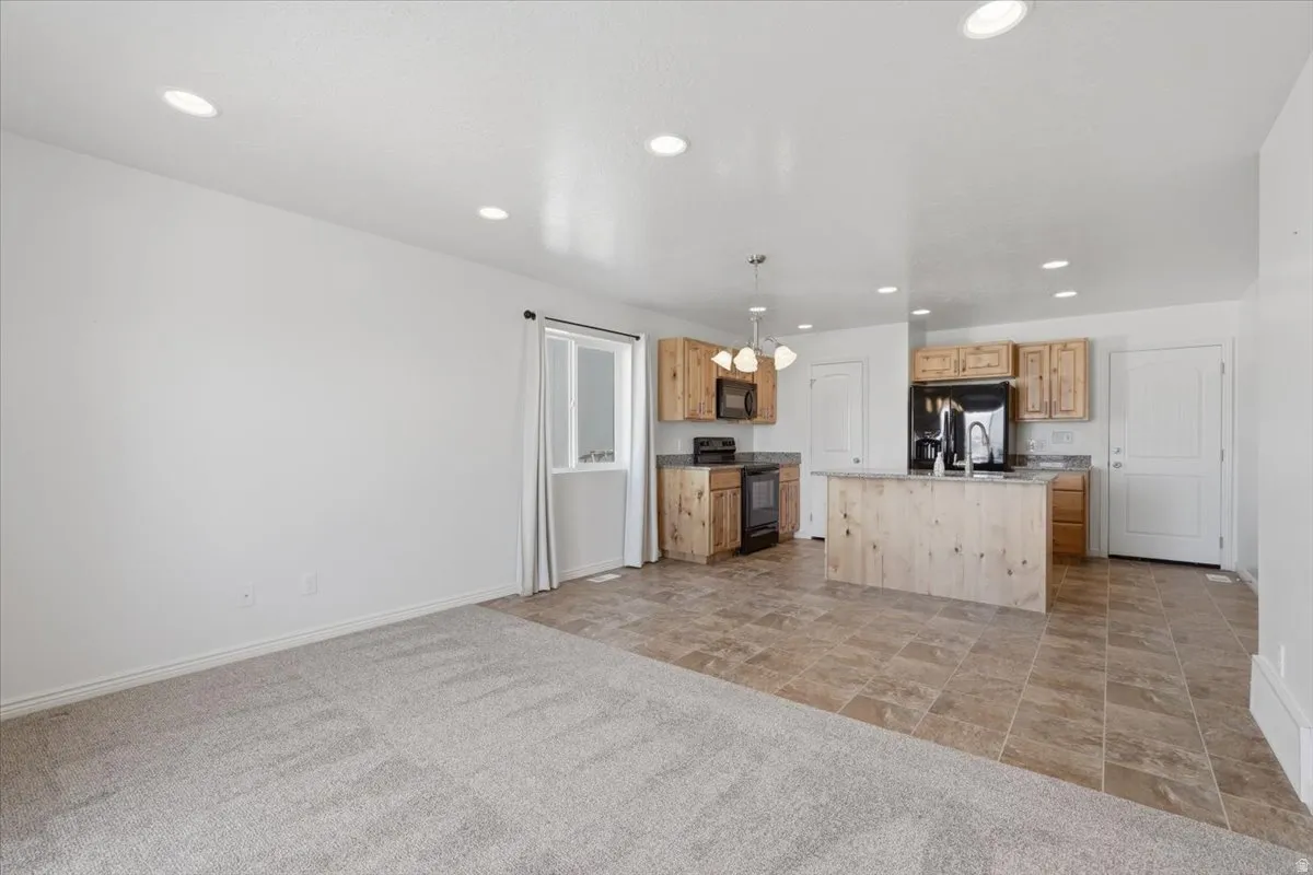 Kitchen featuring black appliances, light wood finish cabinets, light carpet, a center island with sink, and open floor plan