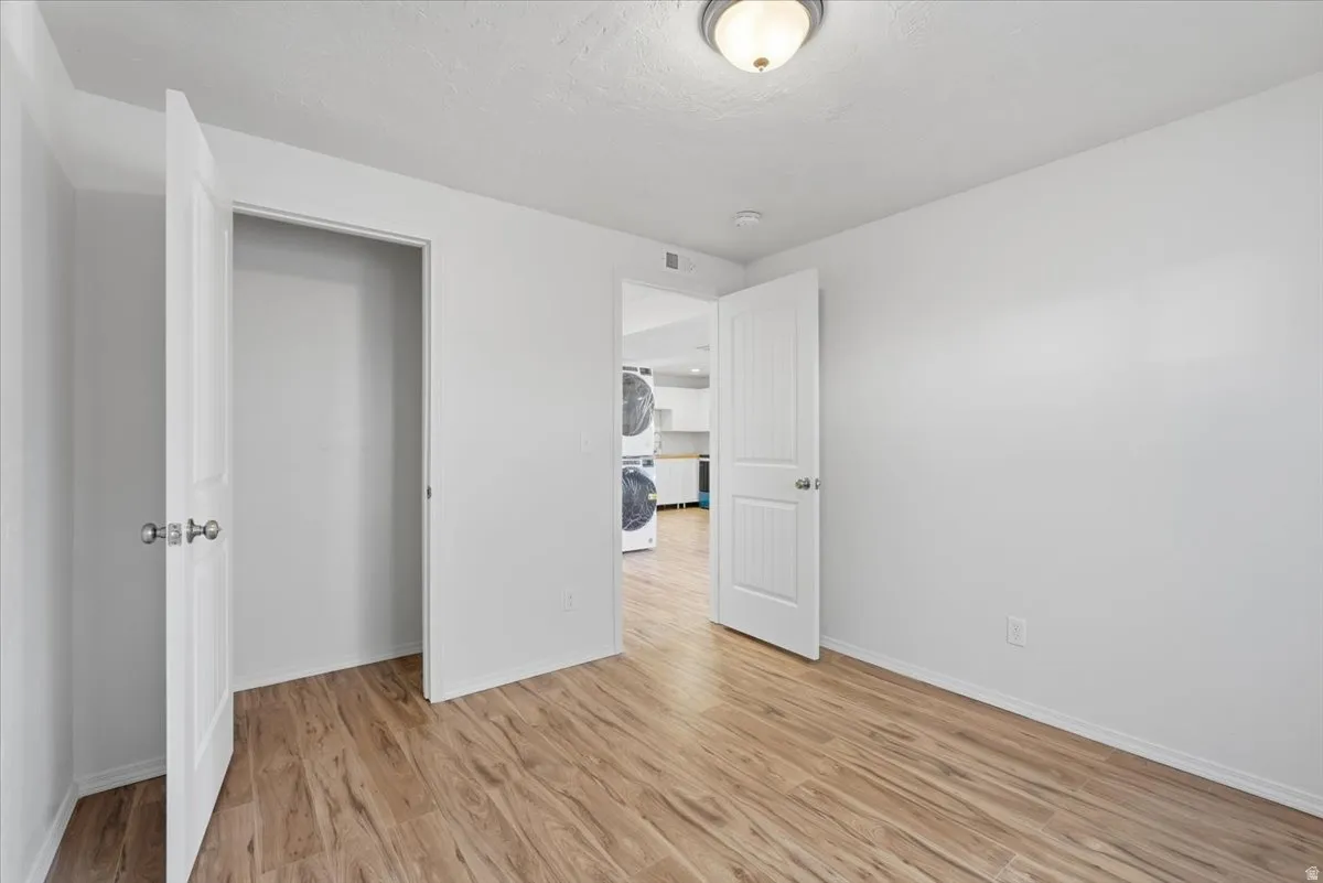 Unfurnished bedroom with light wood-type flooring and stacked washer / drying machine