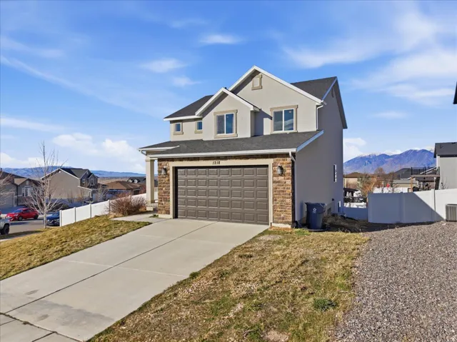 Traditional home with stucco siding, concrete driveway, stone siding, a mountain view, and a residential view