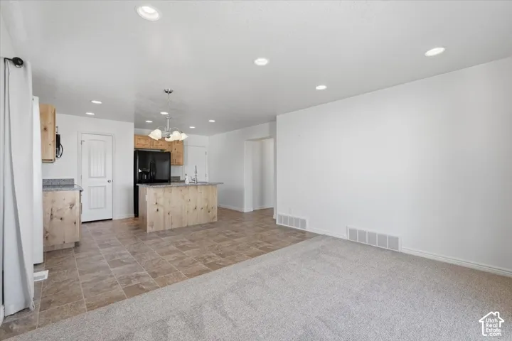 Kitchen with a kitchen island with sink, light wood finish cabinetry, a chandelier, light stone countertops, and stone finish flooring