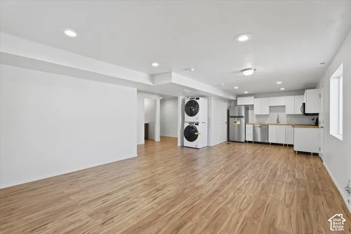Kitchen featuring white cabinets, recessed lighting, light wood-style floors, stacked washer / dryer, and stainless steel appliances