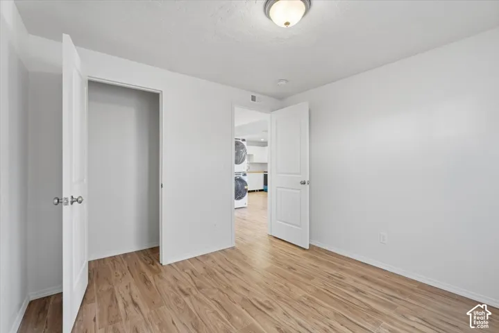 Unfurnished bedroom with light wood-type flooring and stacked washer / drying machine