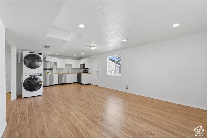 Laundry area with light wood-type flooring, stacked washer and dryer, and recessed lighting