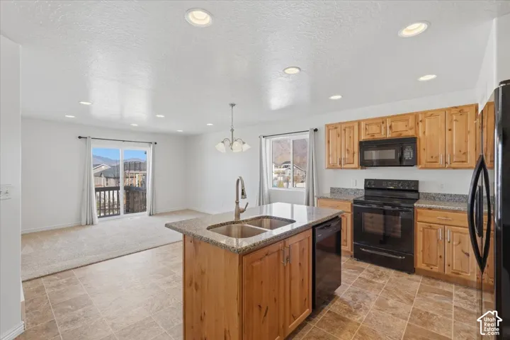 Kitchen featuring black appliances, light stone counters, a textured ceiling, stone finish floors, and a center island with sink
