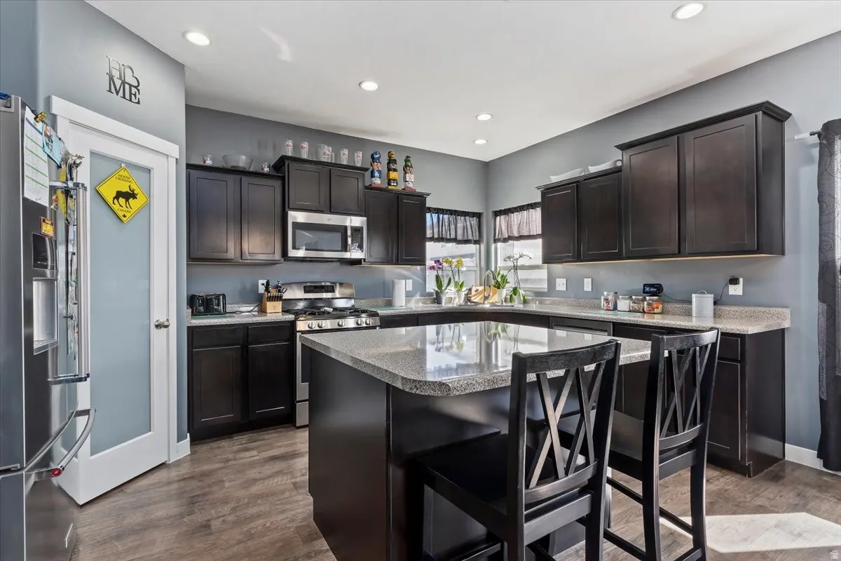 Kitchen featuring a kitchen bar, stainless steel appliances, a kitchen island, dark wood-style floors, and recessed lighting