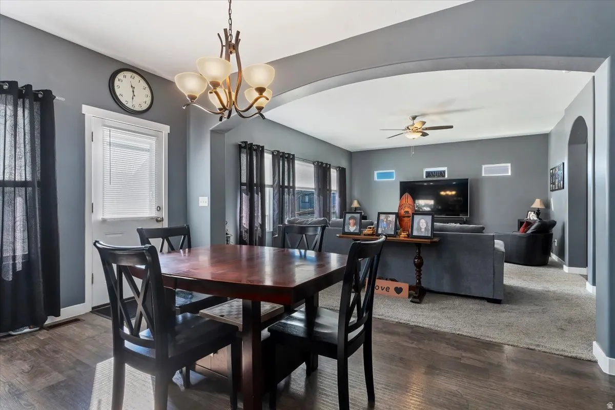 Dining area featuring arched walkways, dark wood-type flooring, ceiling fan, and a chandelier