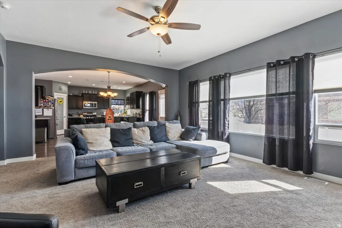 Carpeted living area featuring arched walkways, ceiling fan, and suspended lighting