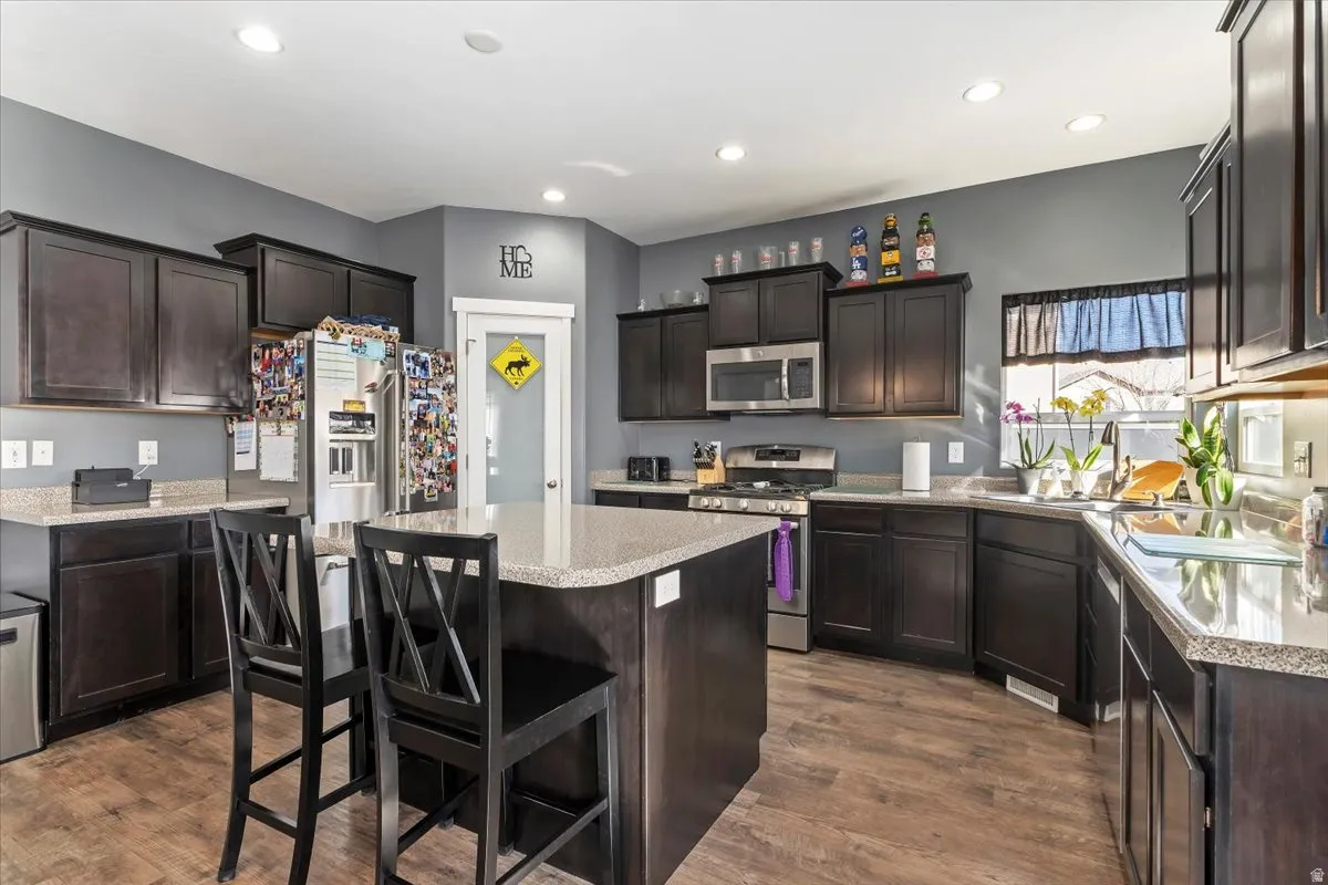 Kitchen with stainless steel appliances, a kitchen bar, a center island, dark wood finish cabinetry, and dark wood-type flooring