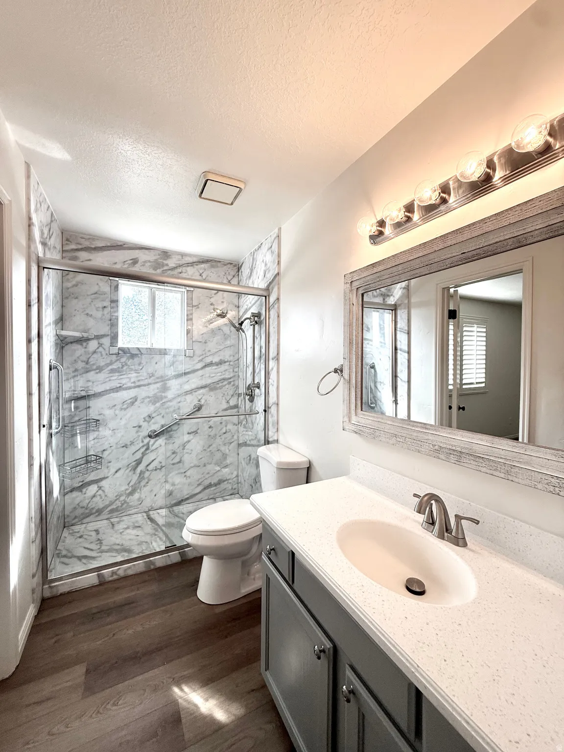 Full bathroom featuring vanity, a marble finish shower, dark wood-type flooring, and a textured ceiling