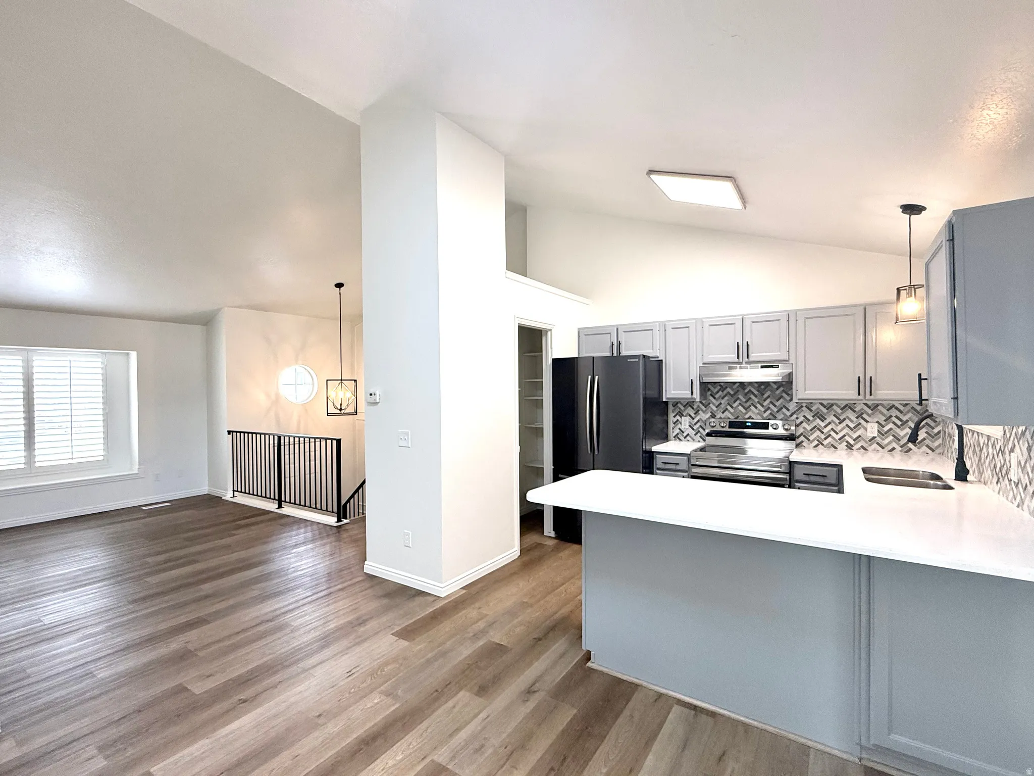 Kitchen with pendant lighting, lofted ceiling, gray cabinets, electric range, and freestanding refrigerator