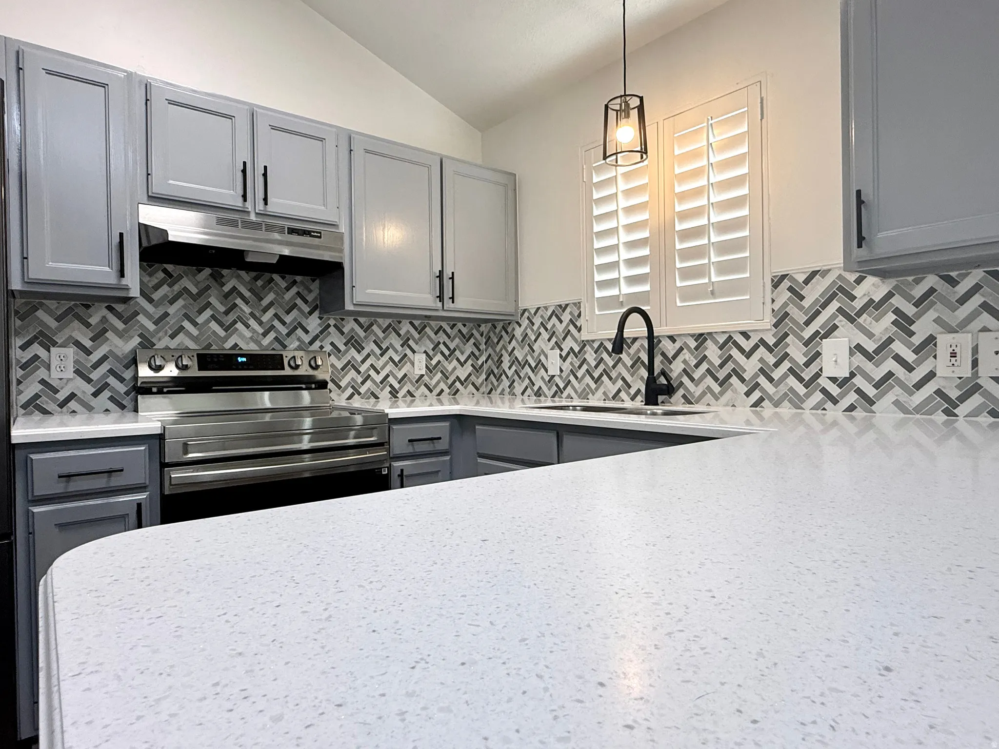 Kitchen with gray cabinets, stainless steel electric range, lofted ceiling, pendant lighting, and decorative backsplash