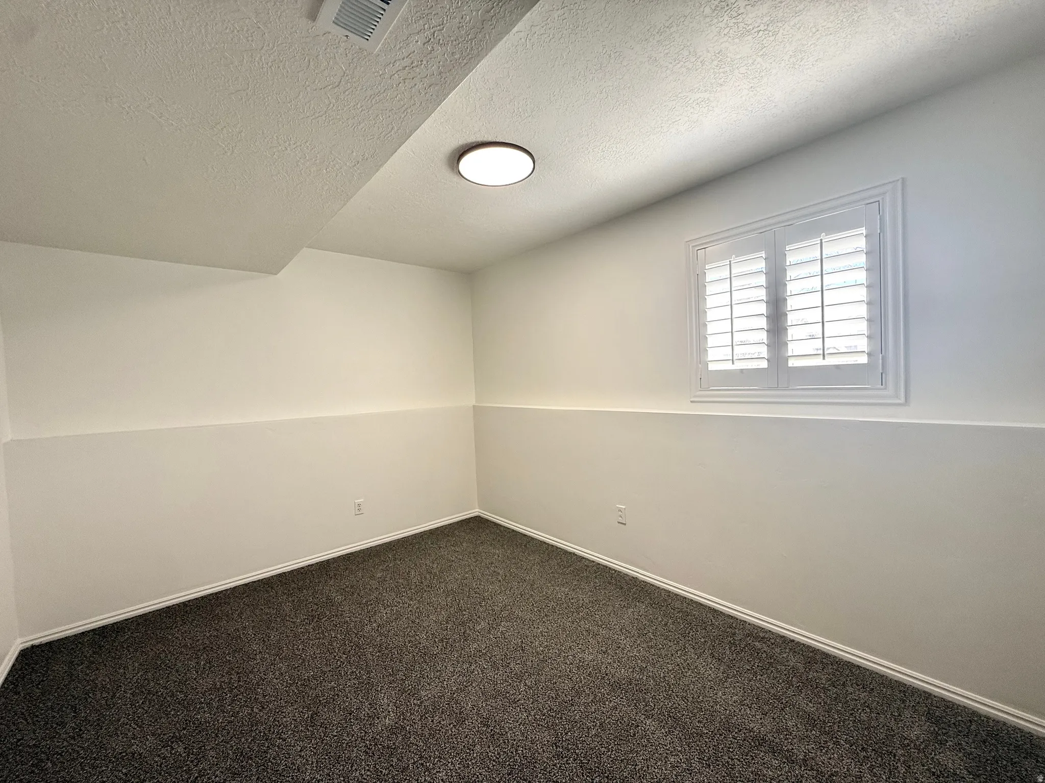 Empty room featuring a textured ceiling and dark colored carpet