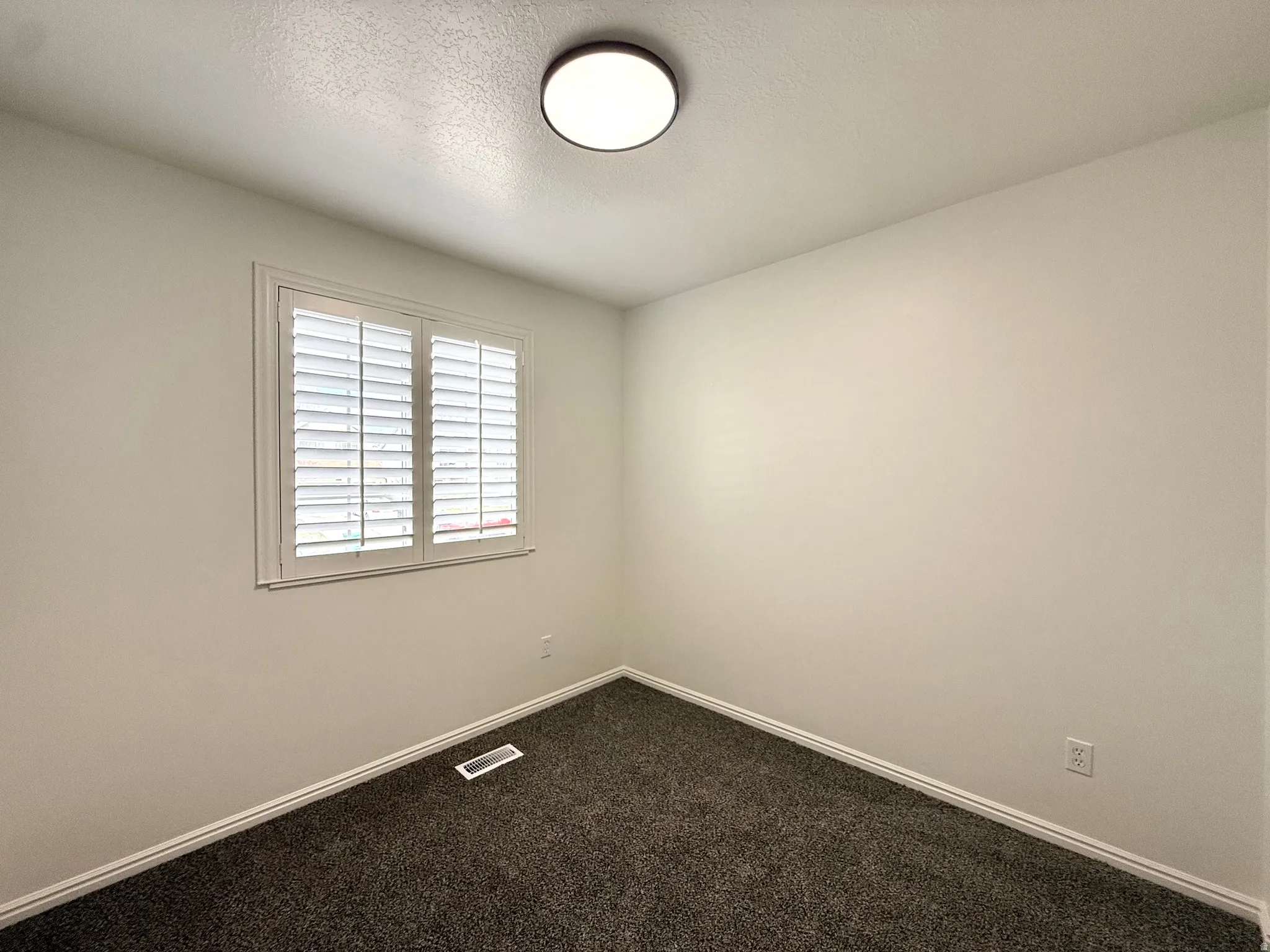 Empty room with dark carpet and a textured ceiling