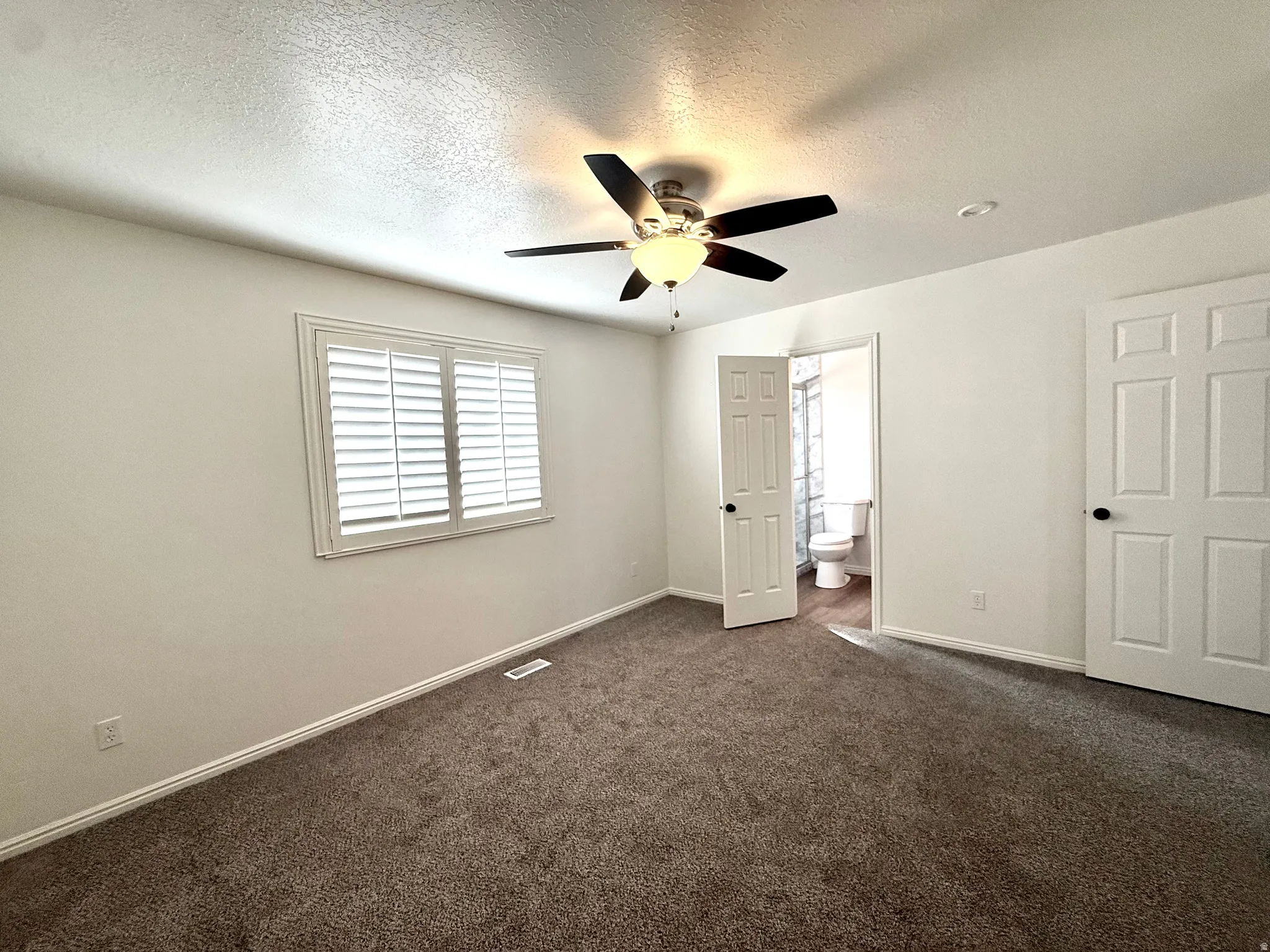 Unfurnished bedroom with dark colored carpet, a textured ceiling, ensuite bathroom, and a ceiling fan