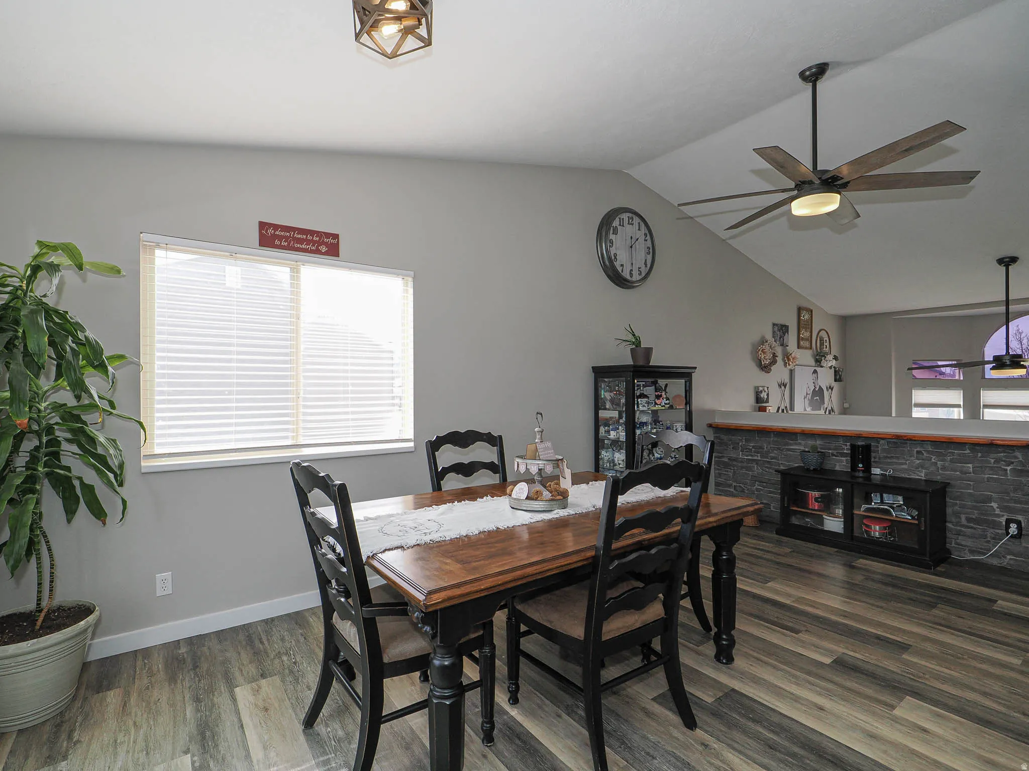 Dining area featuring dark wood finished floors, vaulted ceiling, ceiling fan, and a fireplace