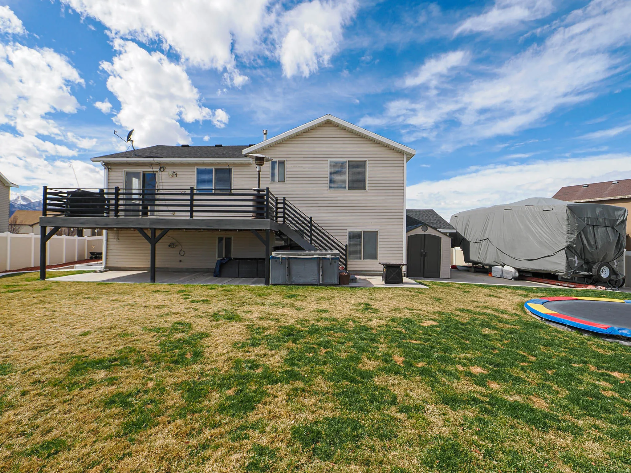 Rear view of house featuring a patio area, a storage unit, a wooden deck, and a jacuzzi