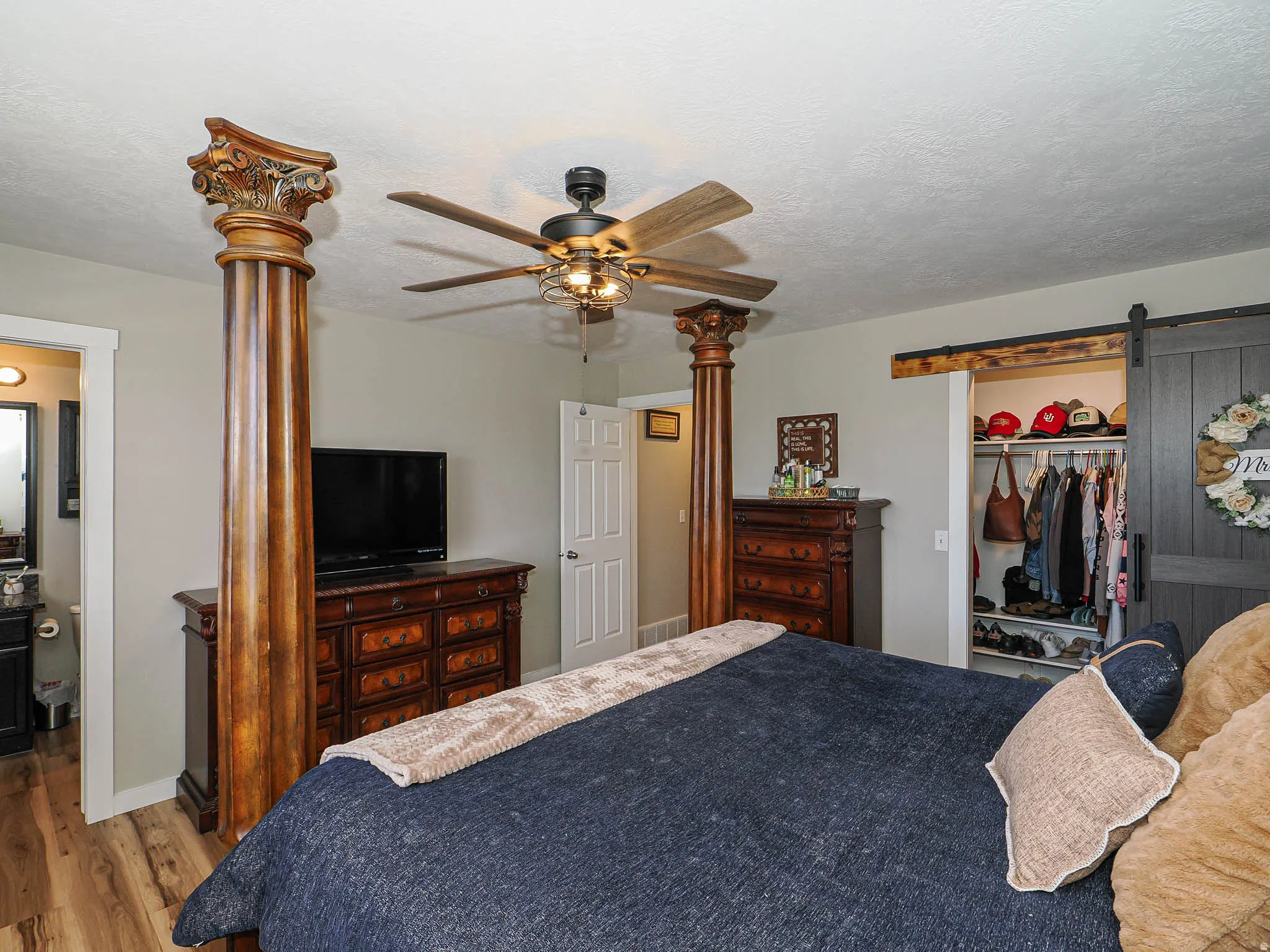 Bedroom featuring a barn door, wood finished floors, a ceiling fan, a textured ceiling, and a walk in closet