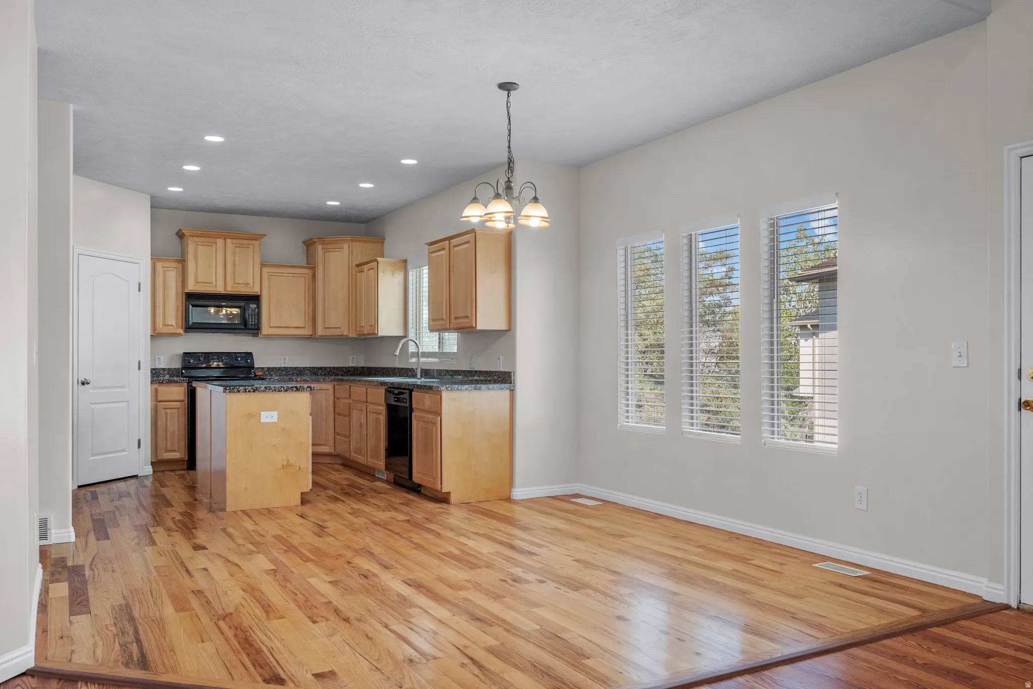Kitchen featuring light wood-type flooring, hanging lights, a kitchen island, dark stone countertops, and black appliances