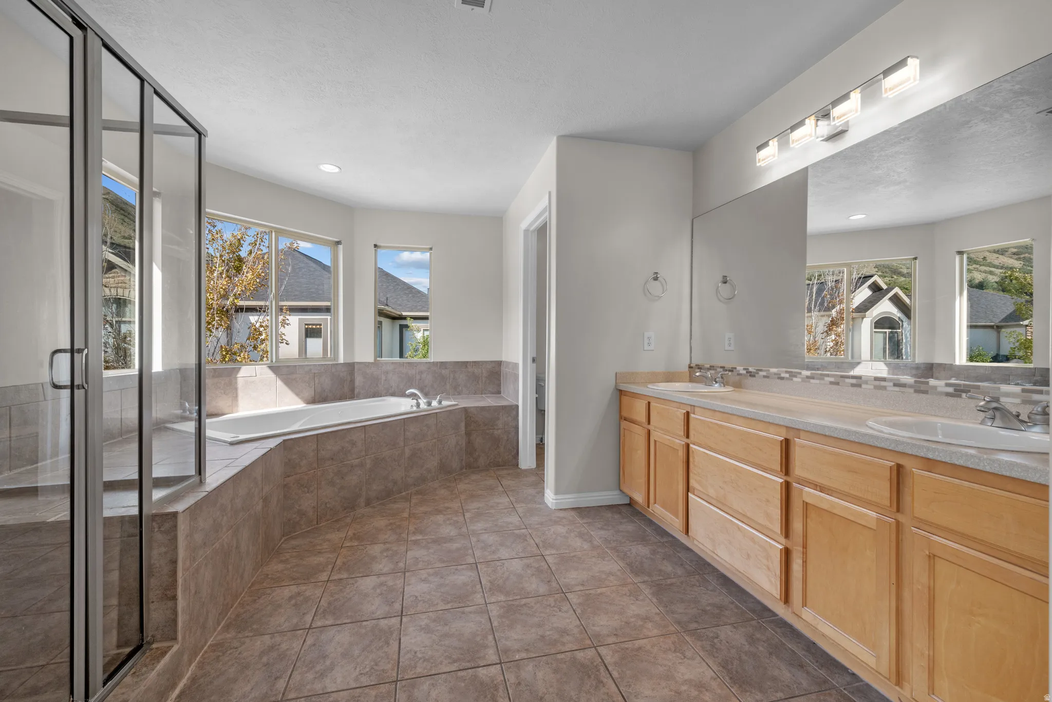 Bathroom featuring double vanity, a garden tub, dark tile patterned flooring, and a shower stall