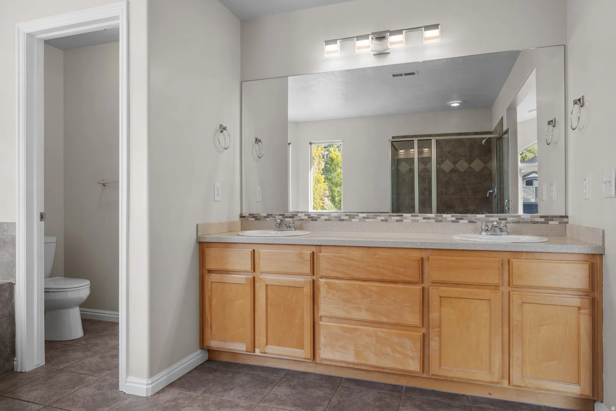 Full bath with double vanity, a stall shower, and dark tile patterned flooring