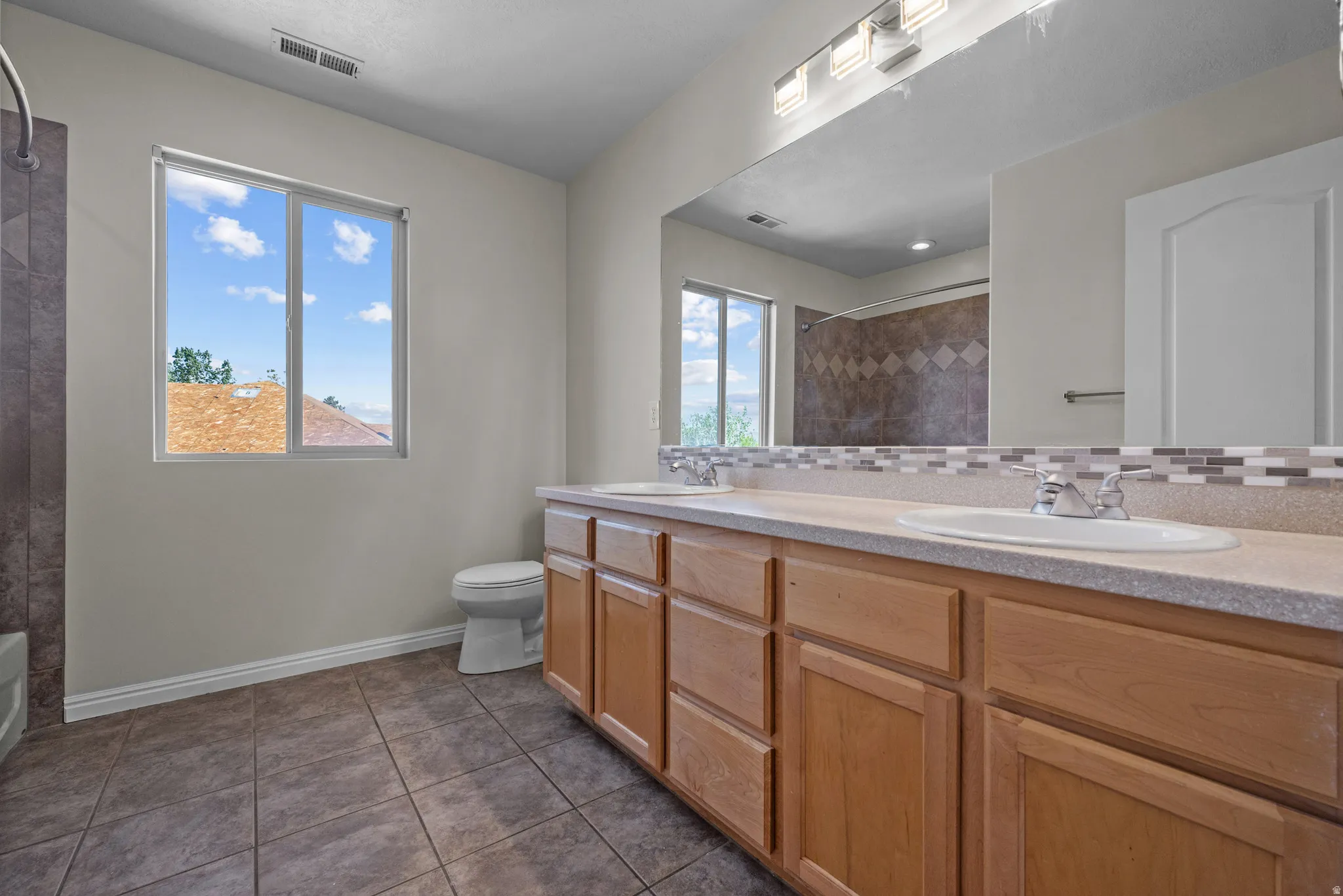 Bathroom with double vanity, dark tile patterned flooring, backsplash, and a shower