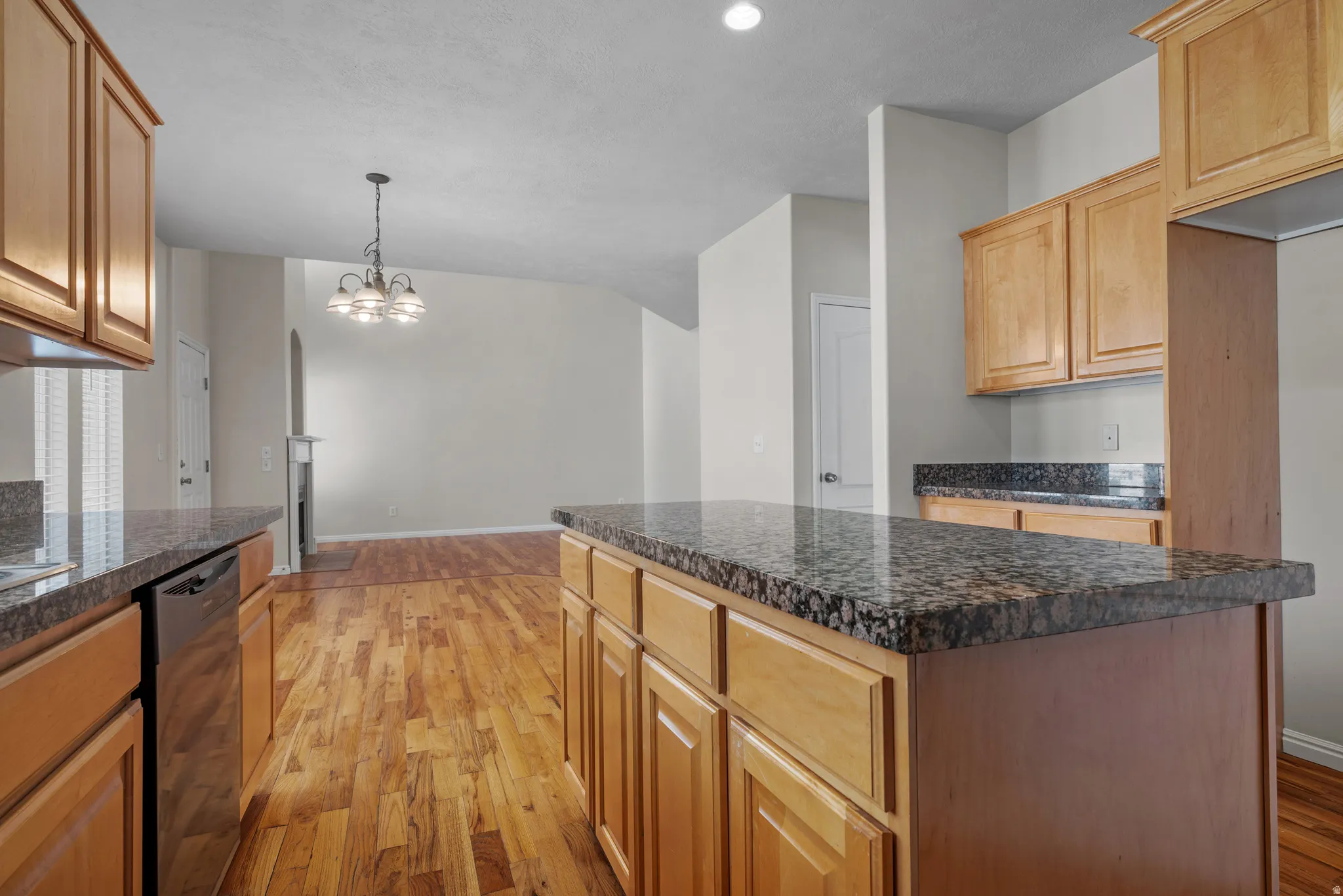 Kitchen with light wood-style floors, black dishwasher, suspended lighting, and a center island