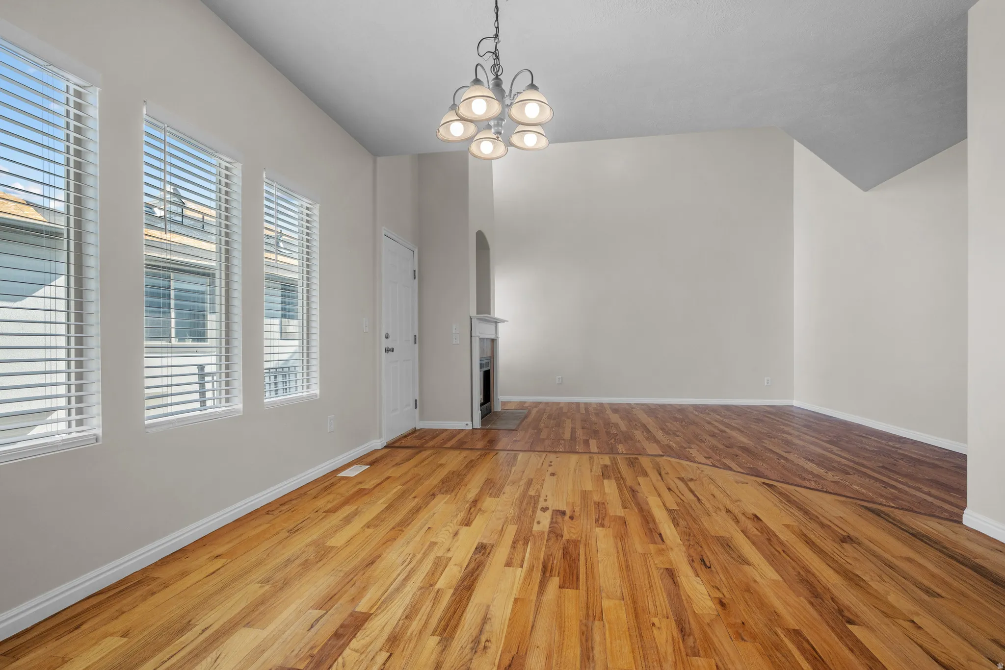 Unfurnished living room featuring light wood finished floors, hanging lights, a fireplace with flush hearth, and arched walkways