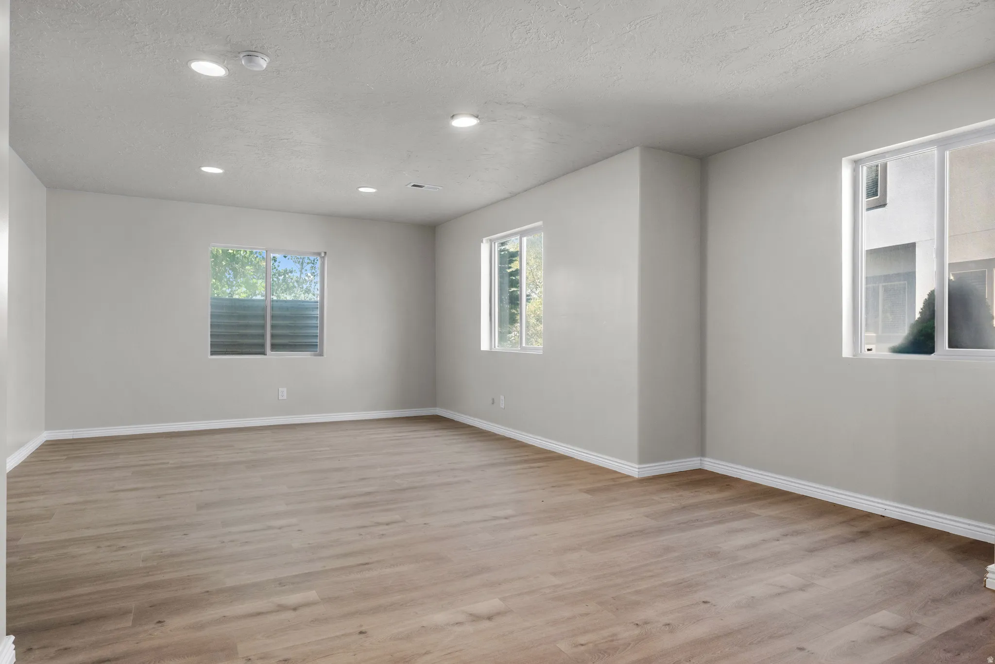 Spare room with light wood-style flooring, healthy amount of natural light, a textured ceiling, and recessed lighting