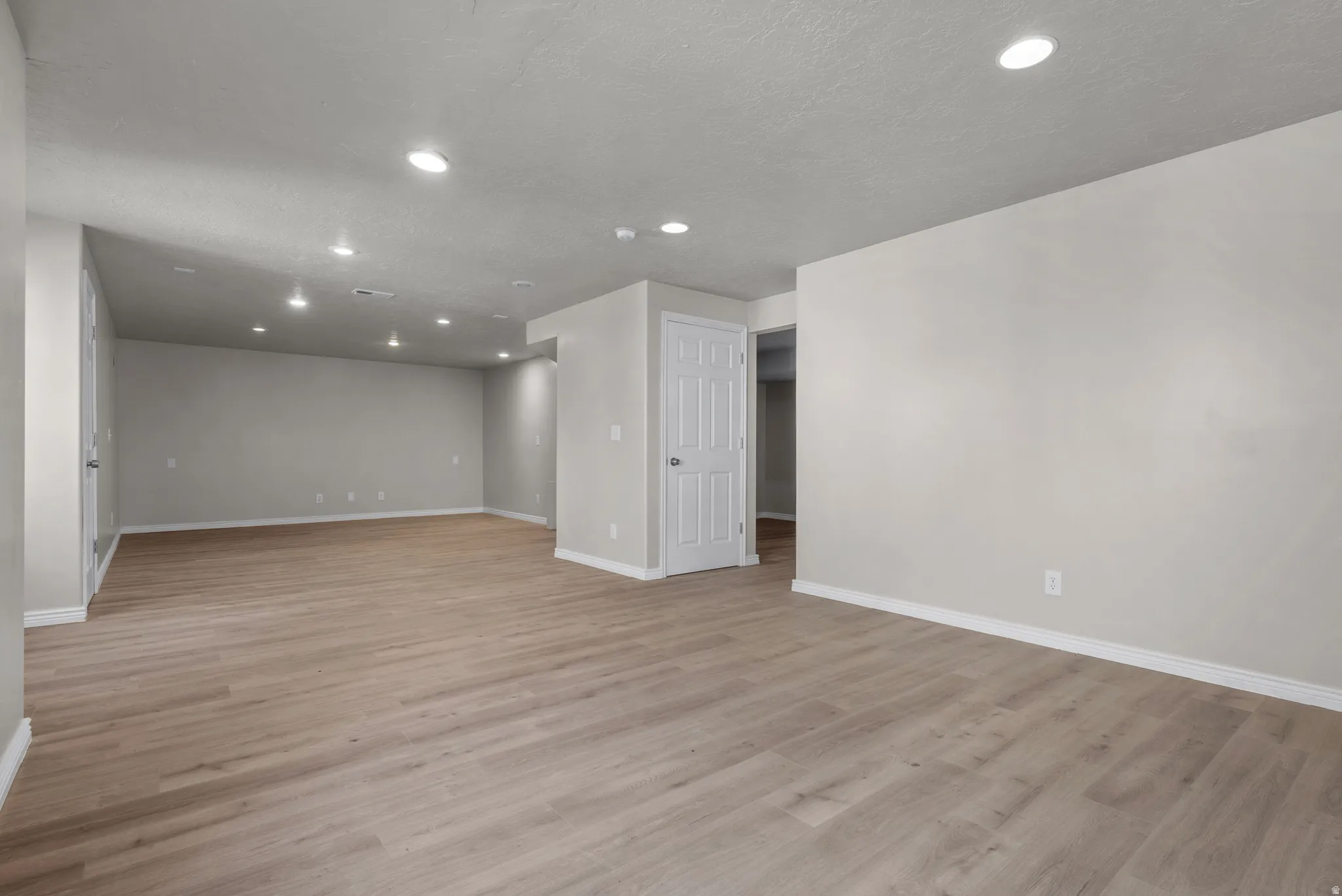 Empty room with light wood-style floors and recessed lighting