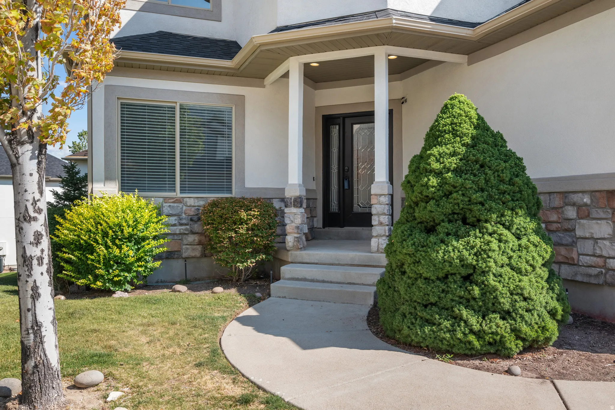 Doorway to property featuring stone siding, stucco siding, a lawn, and roof with shingles