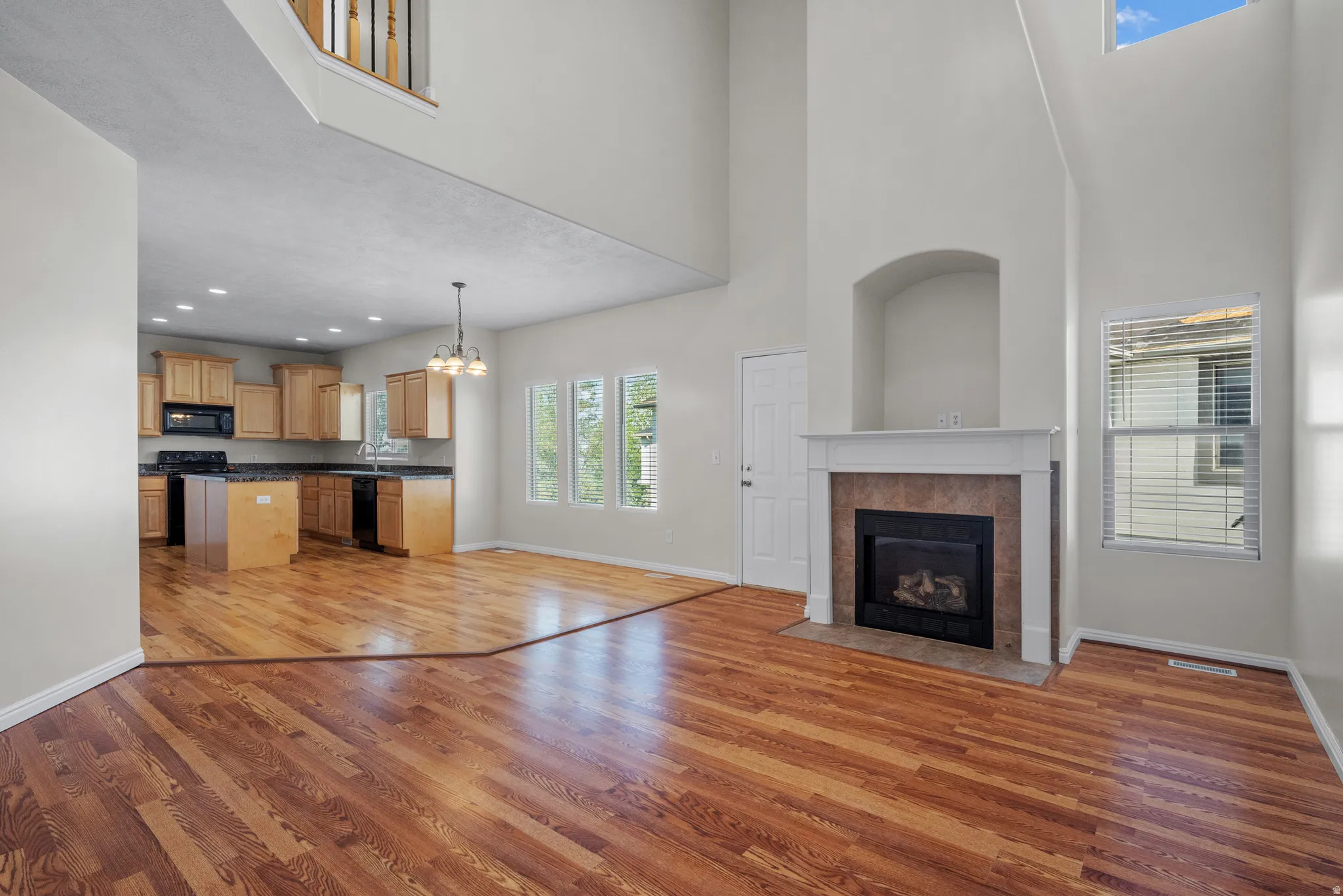 Unfurnished living room with light wood-style floors, suspended lighting, a tiled fireplace, and a high ceiling