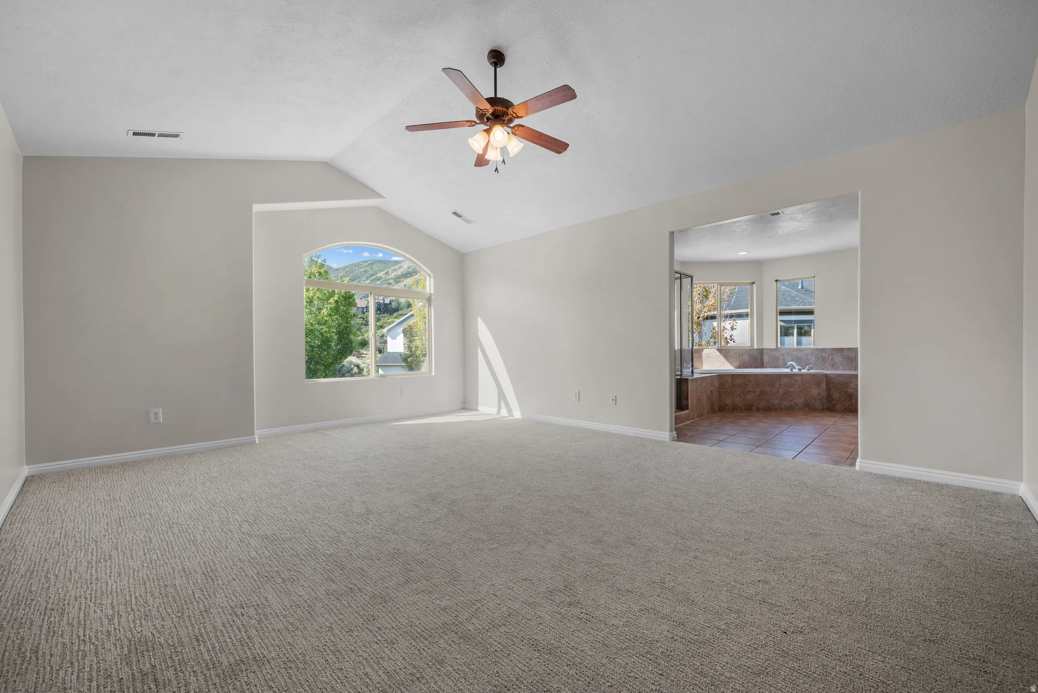 Unfurnished room featuring a ceiling fan, light carpet, vaulted ceiling, and healthy amount of natural light