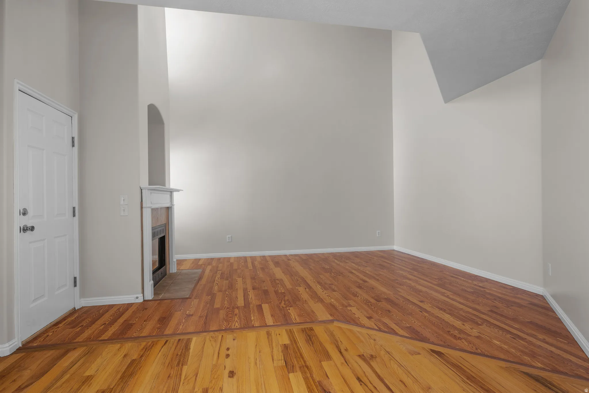 Unfurnished living room with light wood-type flooring, a tile fireplace, a high ceiling, and arched walkways
