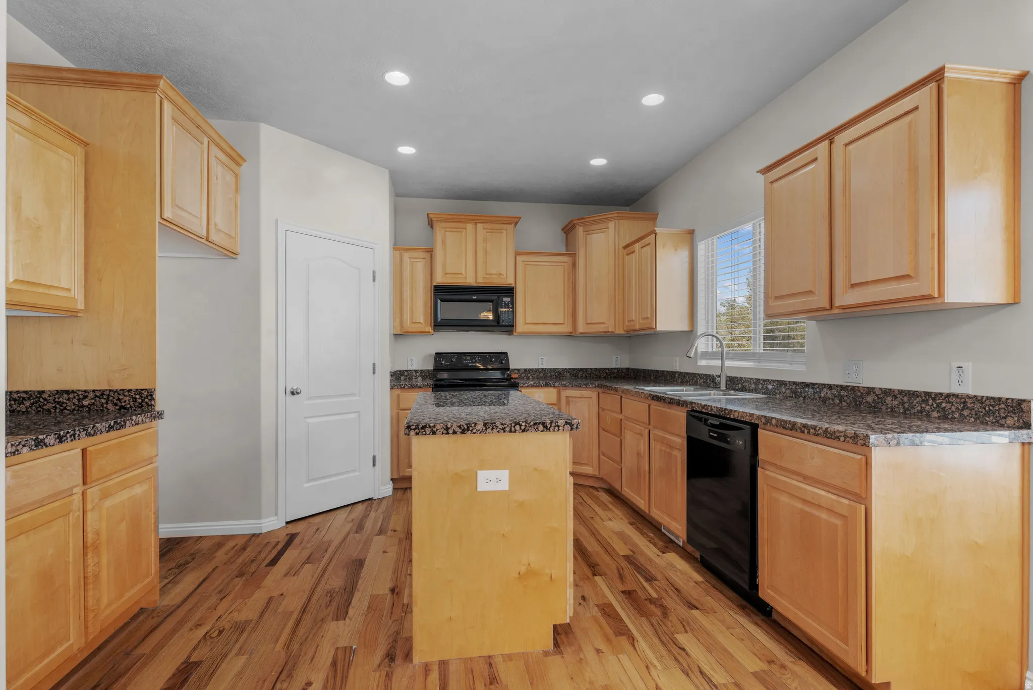 Kitchen featuring light wood finish cabinets, black appliances, a kitchen island, light wood-style floors, and recessed lighting