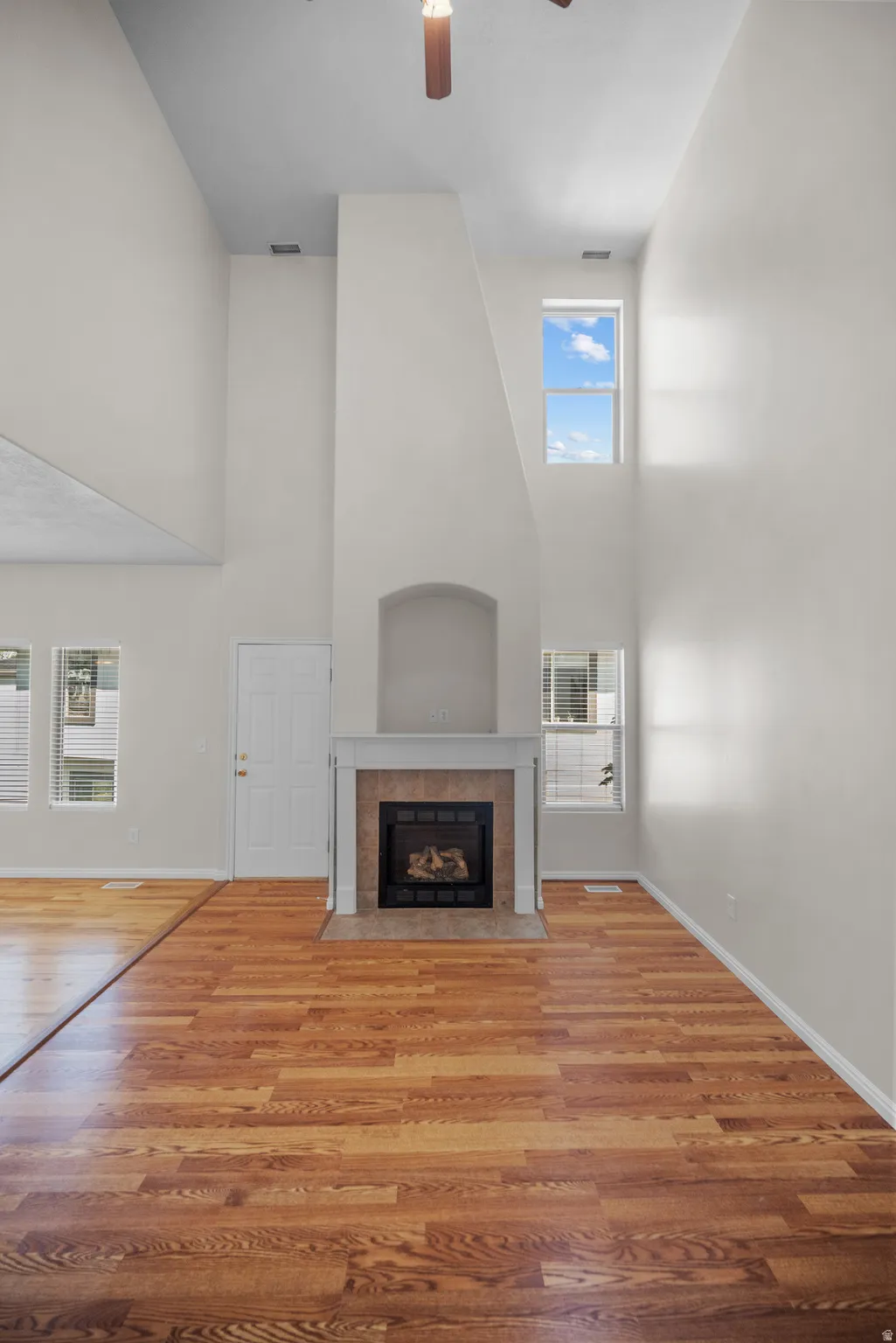 Unfurnished living room featuring a high ceiling, a tiled fireplace, ceiling fan, and light wood-type flooring
