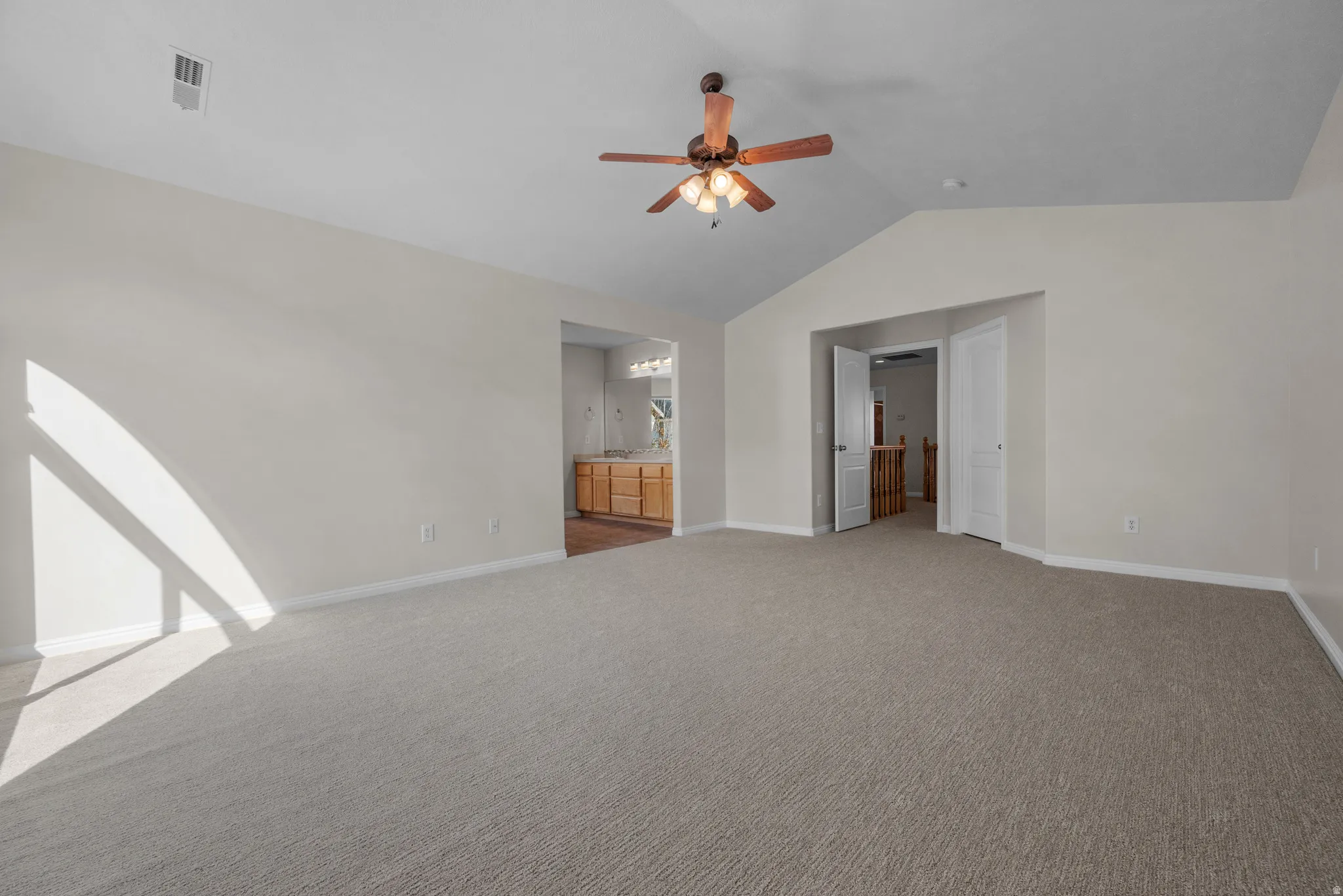 Unfurnished bedroom featuring light carpet, ceiling fan, and ensuite bath