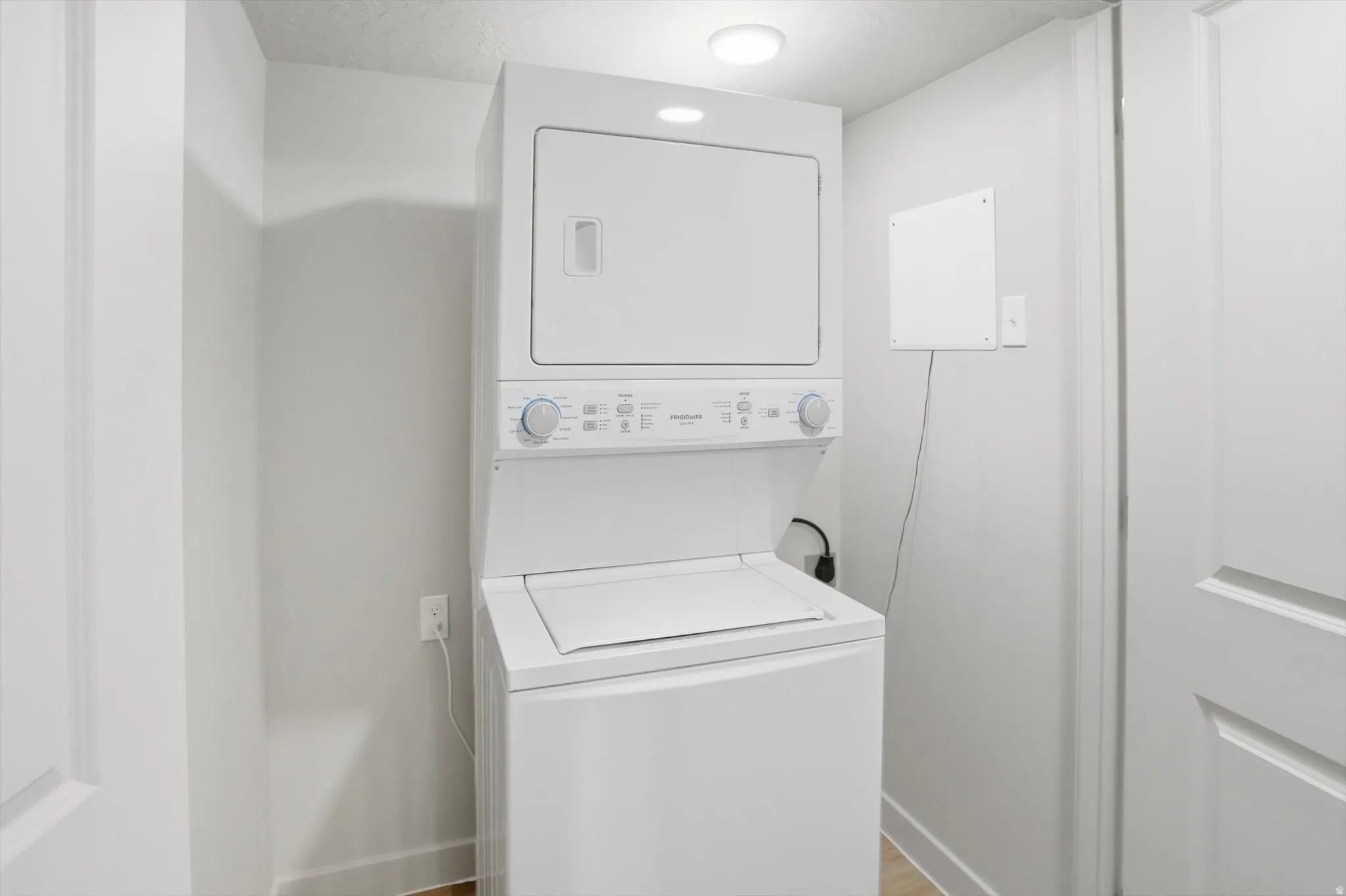 Laundry area with stacked washer / drying machine and light wood-style floors