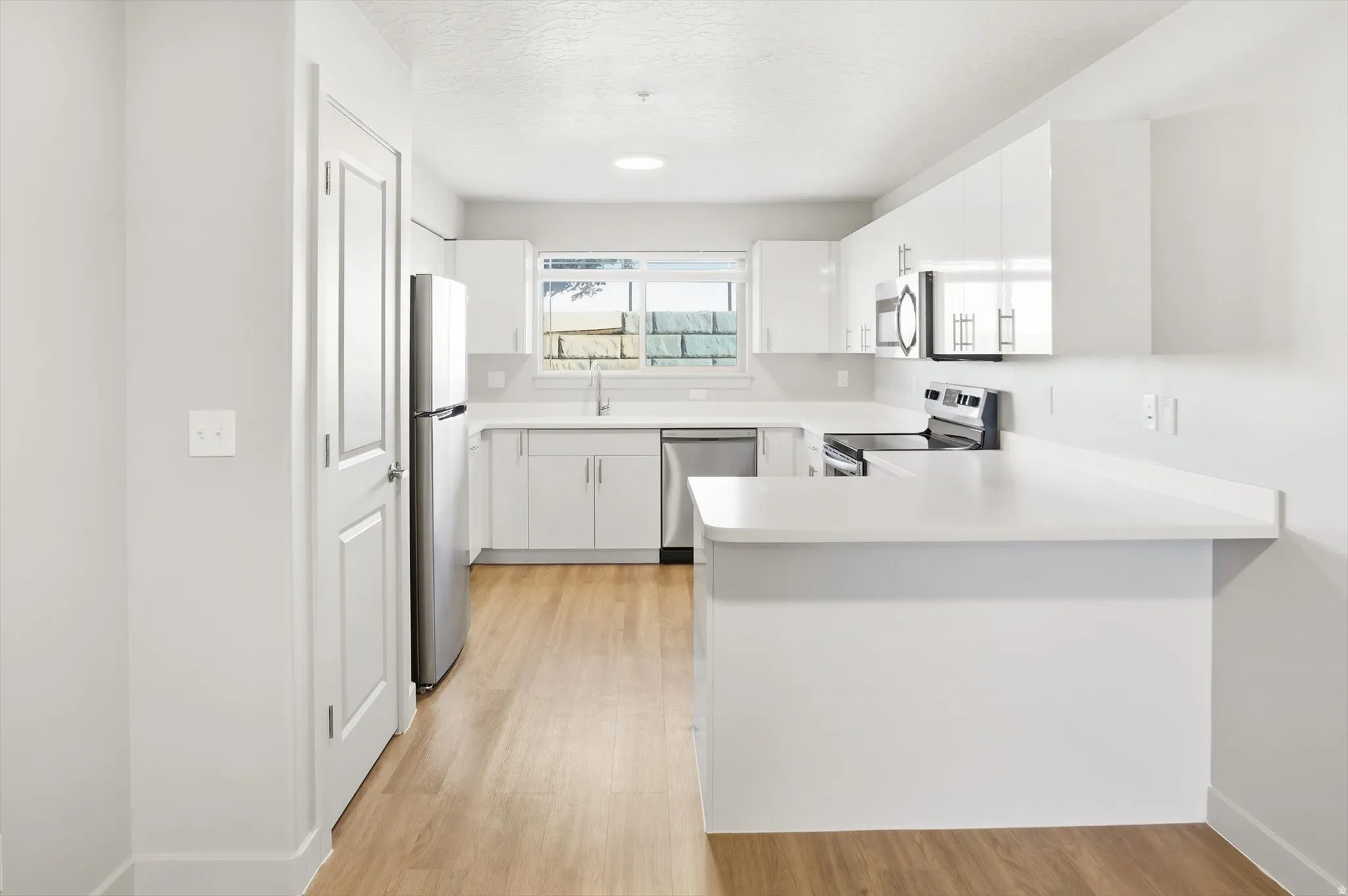Kitchen featuring light countertops, white cabinets, stainless steel appliances, a peninsula, and light wood-style flooring