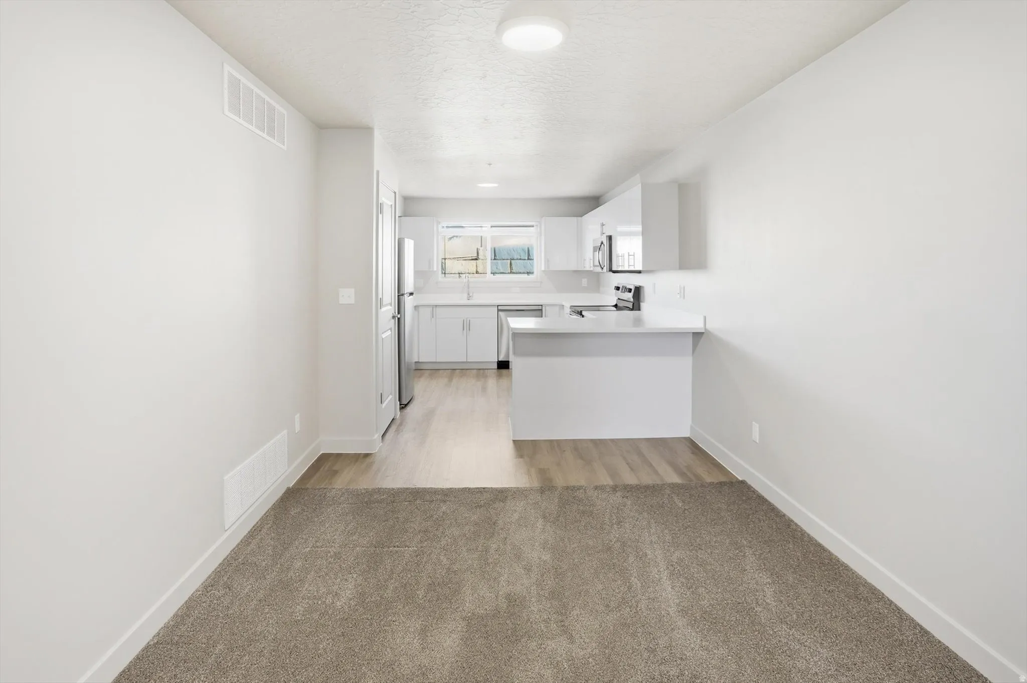 Kitchen featuring a peninsula, light countertops, white cabinets, light carpet, and stainless steel appliances