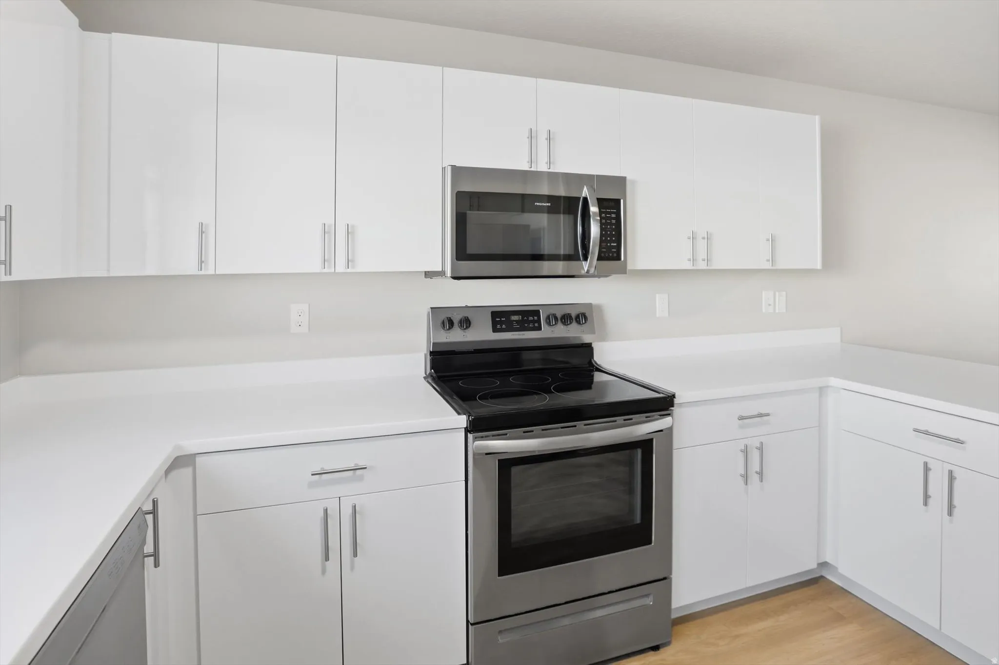 Kitchen featuring stainless steel appliances, white cabinets, light countertops, and light wood-style flooring