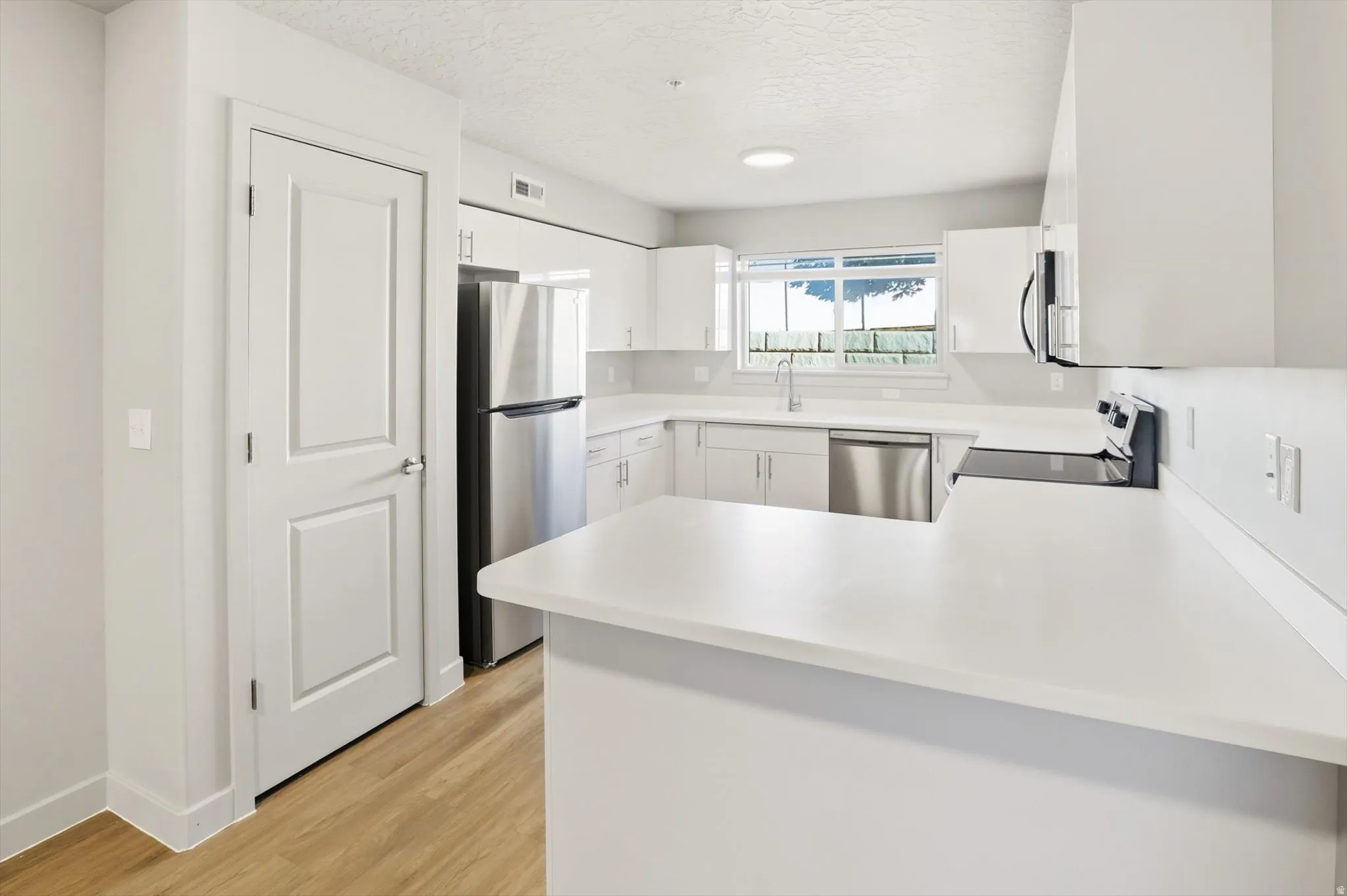 Kitchen with stainless steel appliances, light countertops, white cabinets, light wood finished floors, and a peninsula