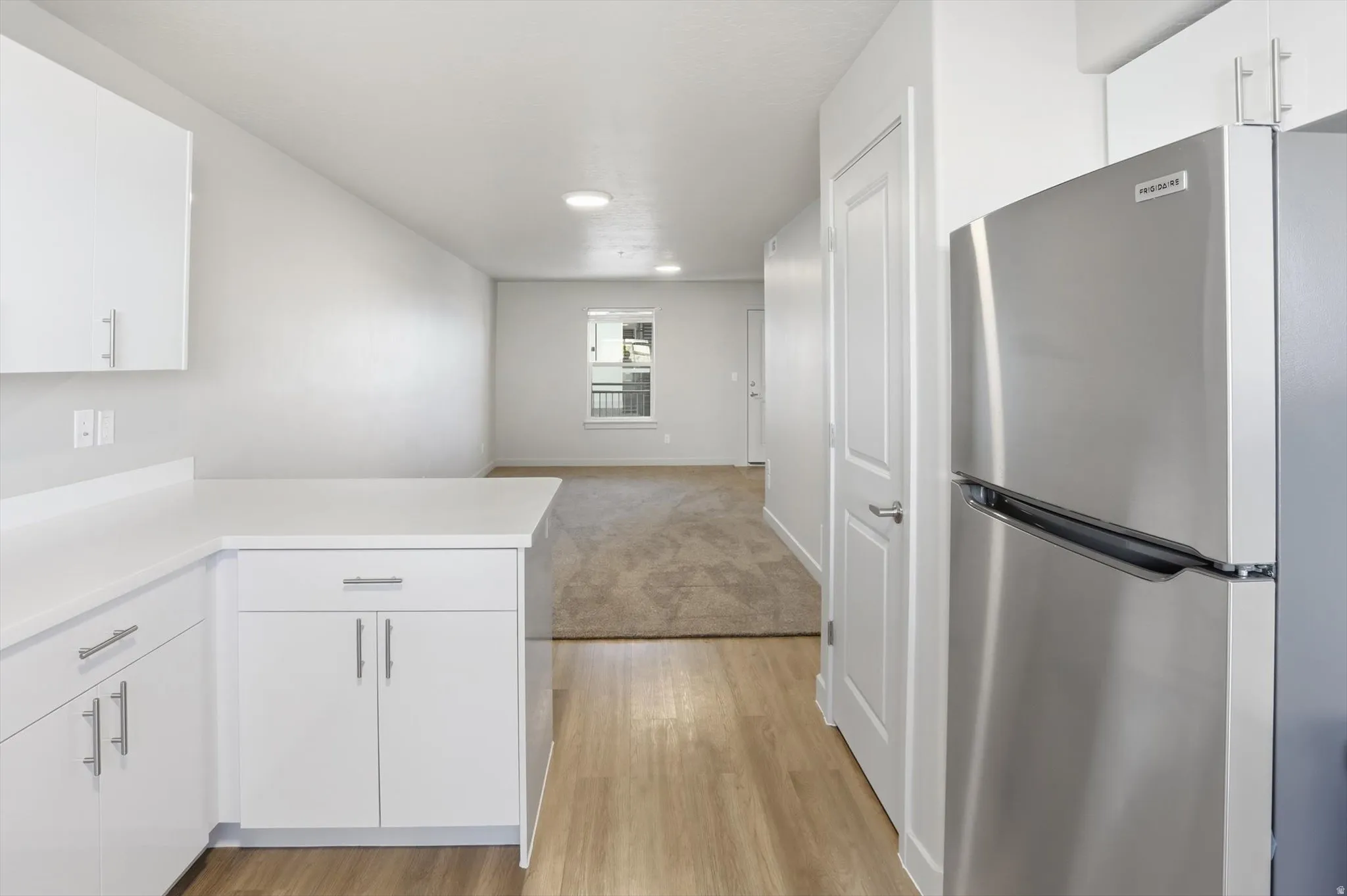 Kitchen with white cabinets, freestanding refrigerator, light countertops, light wood-style floors, and light carpet