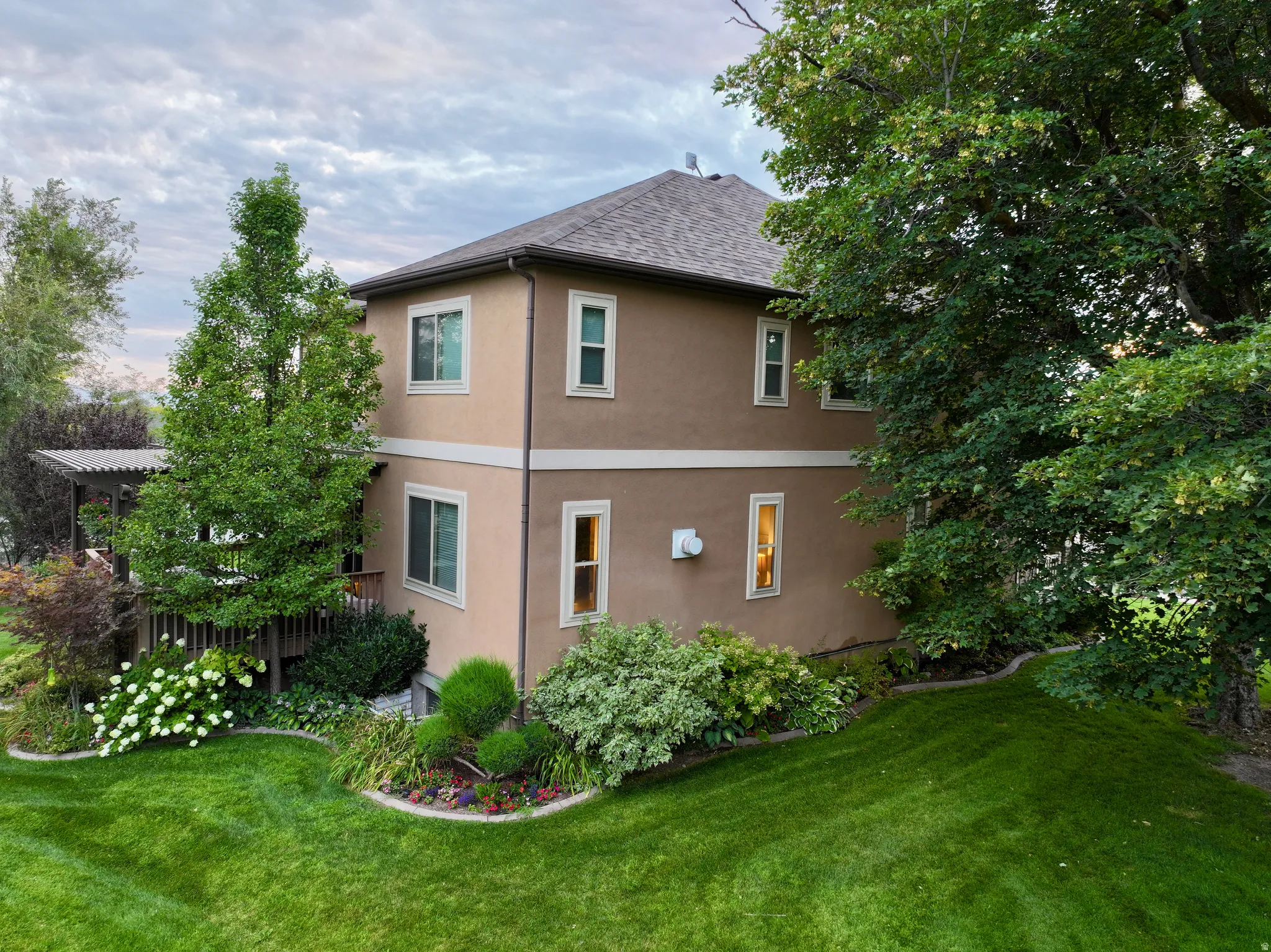 View of property exterior with a mature landscape, stucco siding, and a new shingled roof