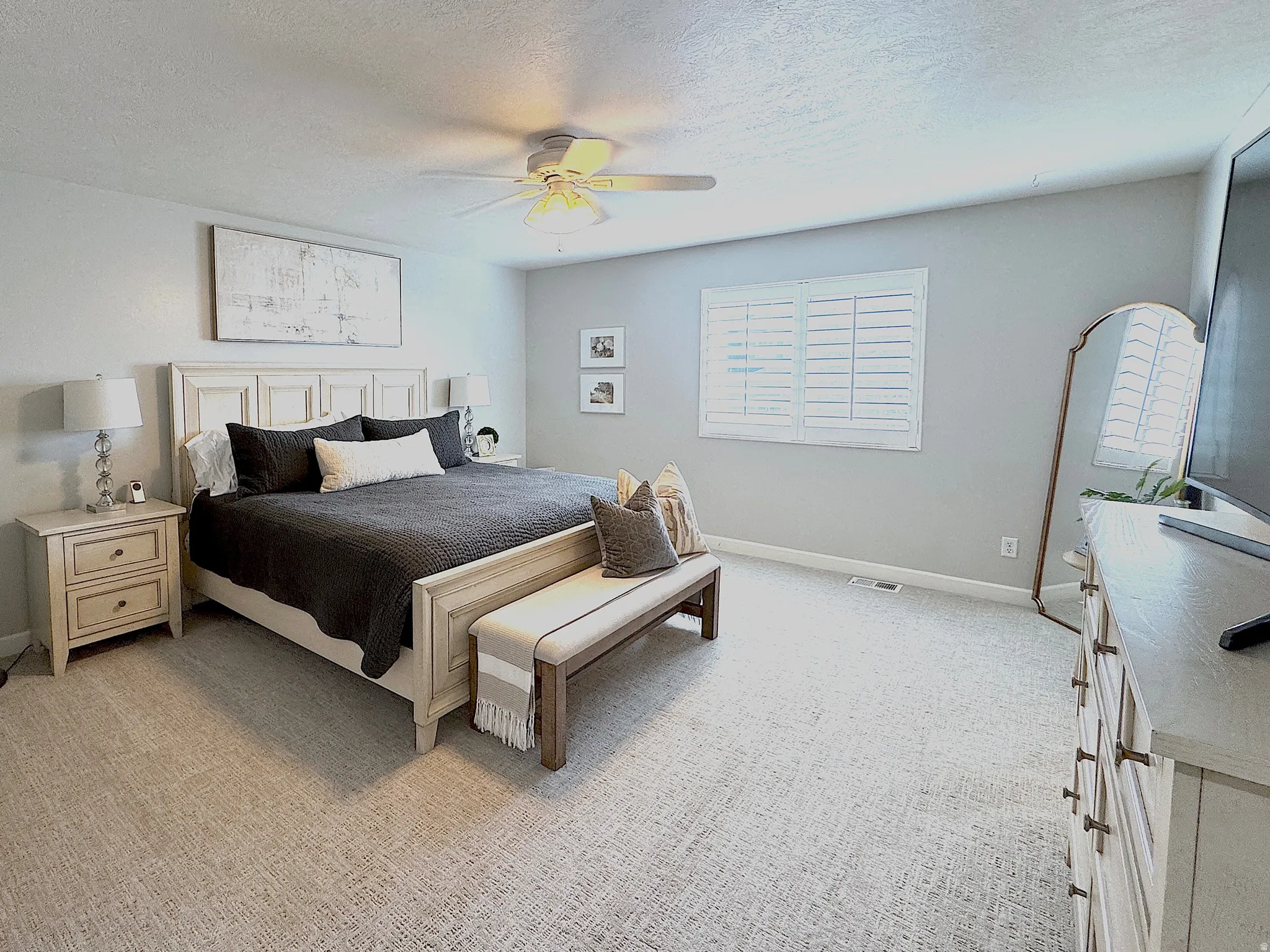 Spacious master bedroom with light carpet and ceiling fan