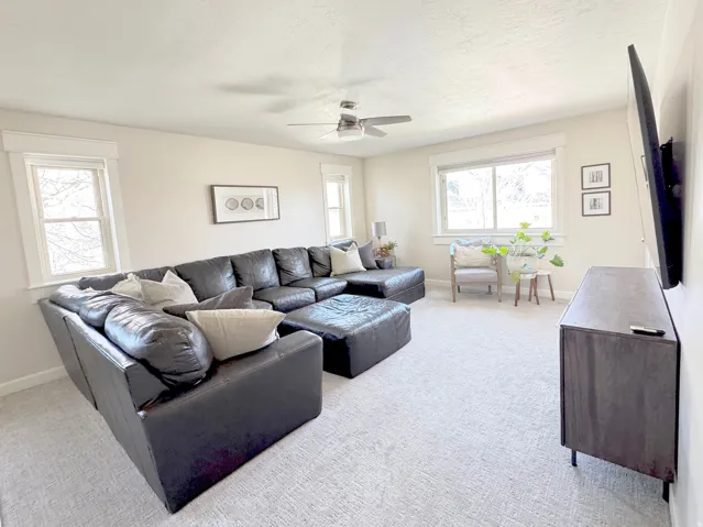 Living area featuring light carpet, a ceiling fan, and lots of natural light